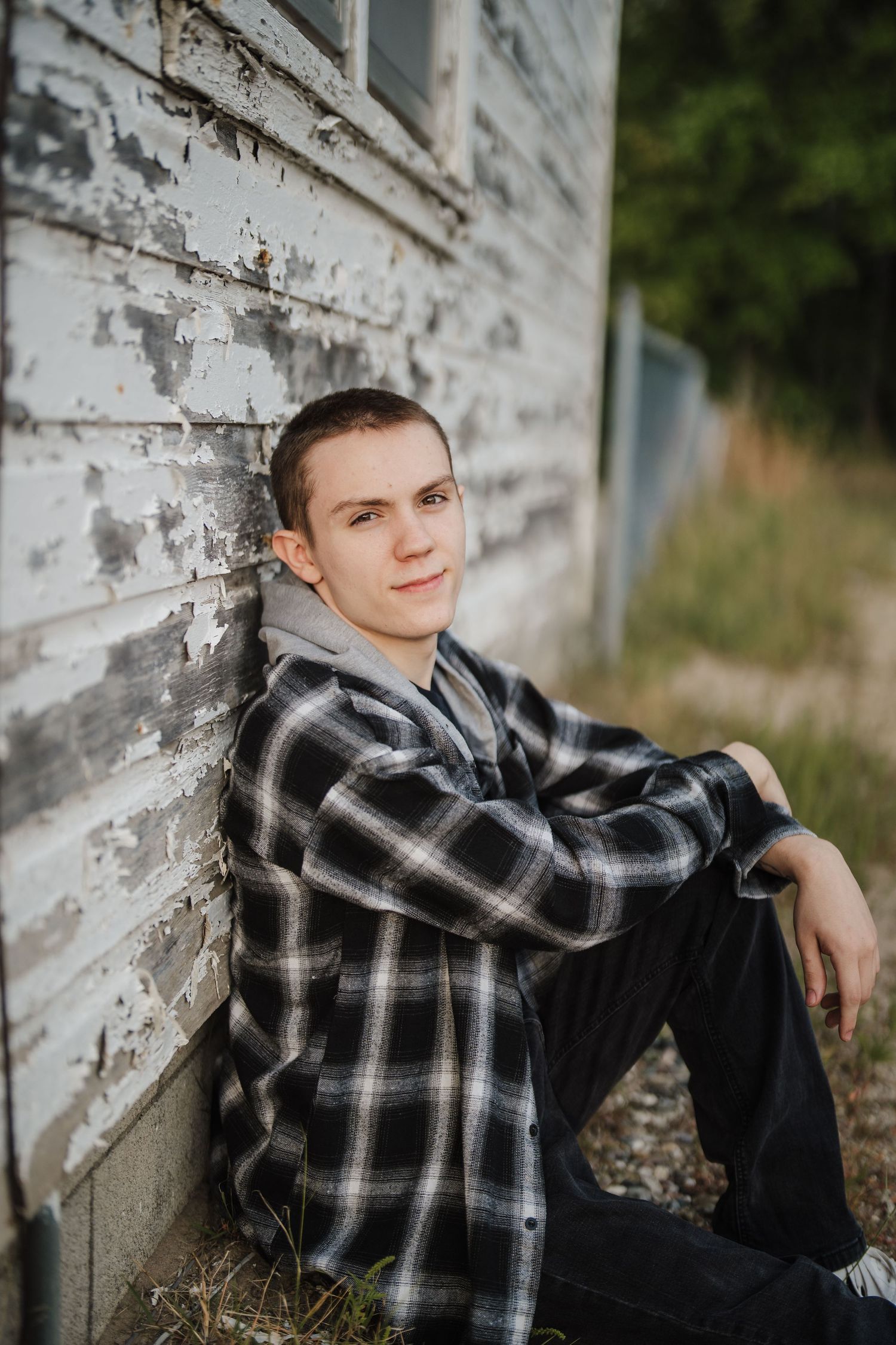 Casual portrait against weathered white building exterior wearing plaid flannel shirt and dark pants.