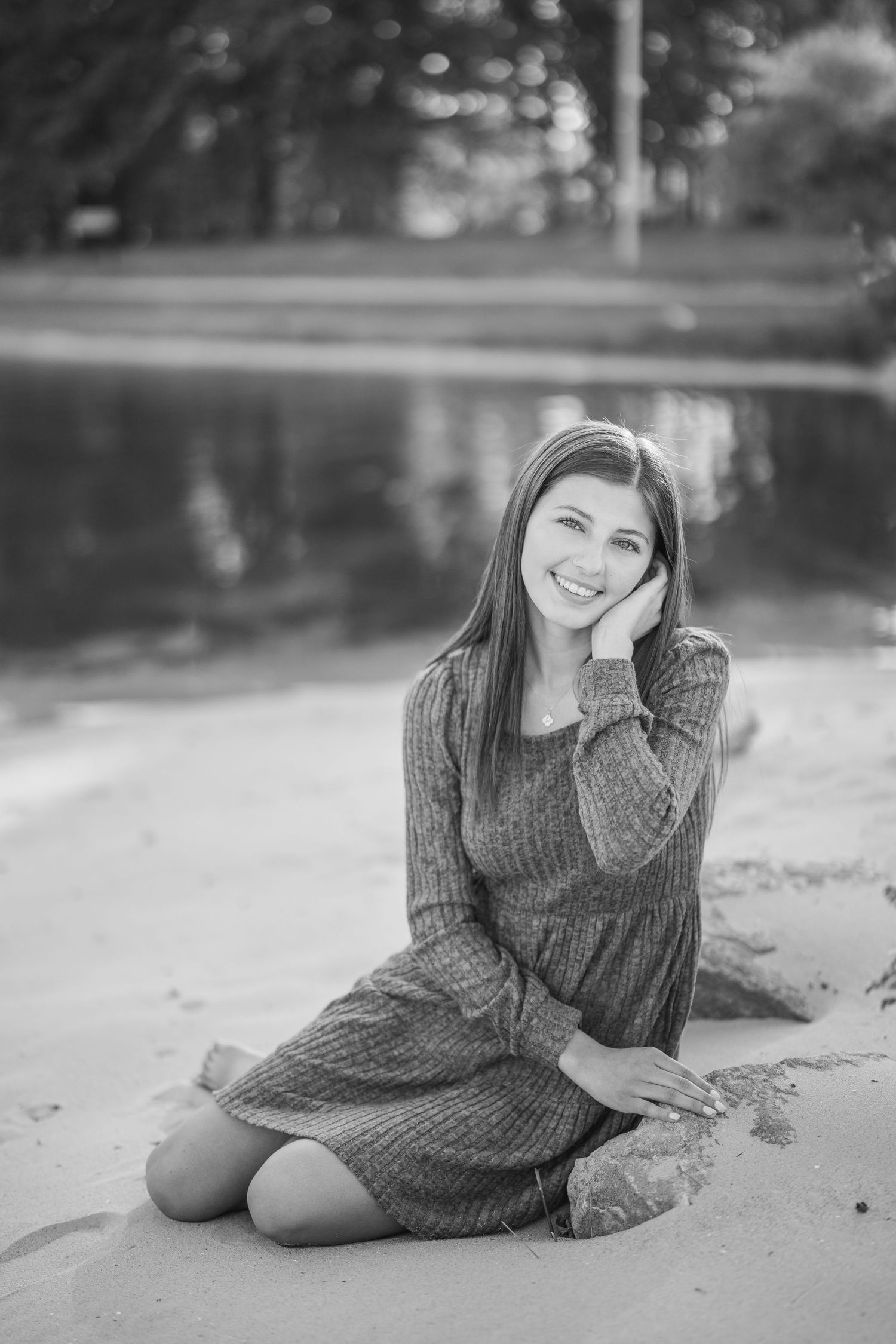 A black and white portrait of someone laying on a sandy beach in a sweater dress.