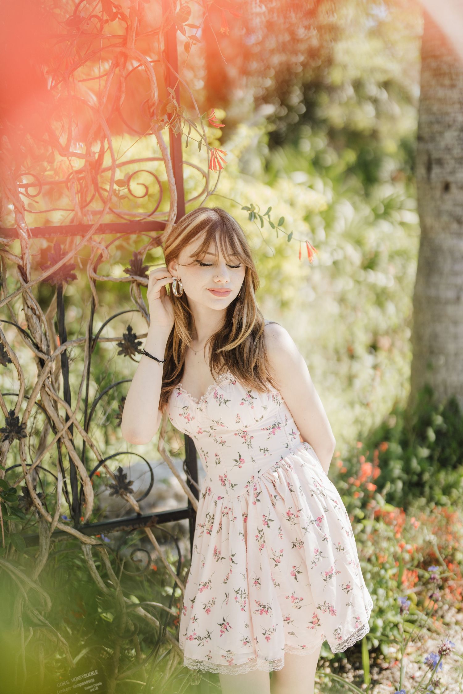 Whimsical outdoor portrait with coral-tinted lighting among blooming flowers and garden foliage.
