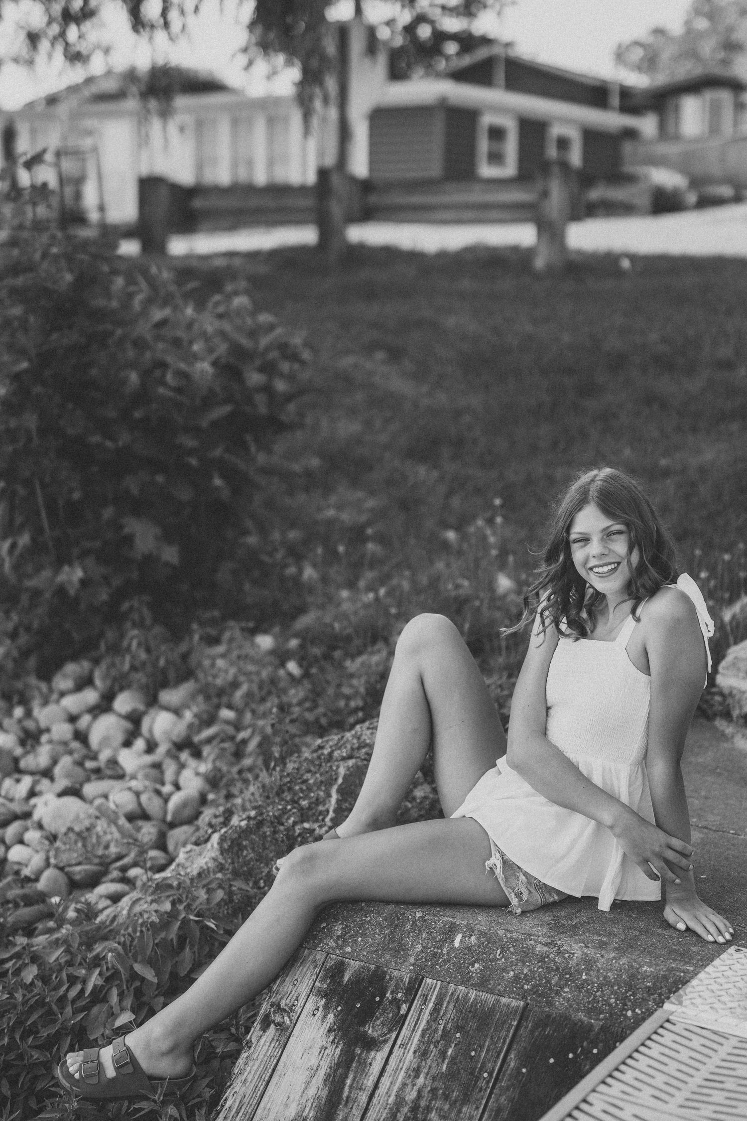 Black and white artistic portrait showing someone lying on a wooden surface in a garden setting.
