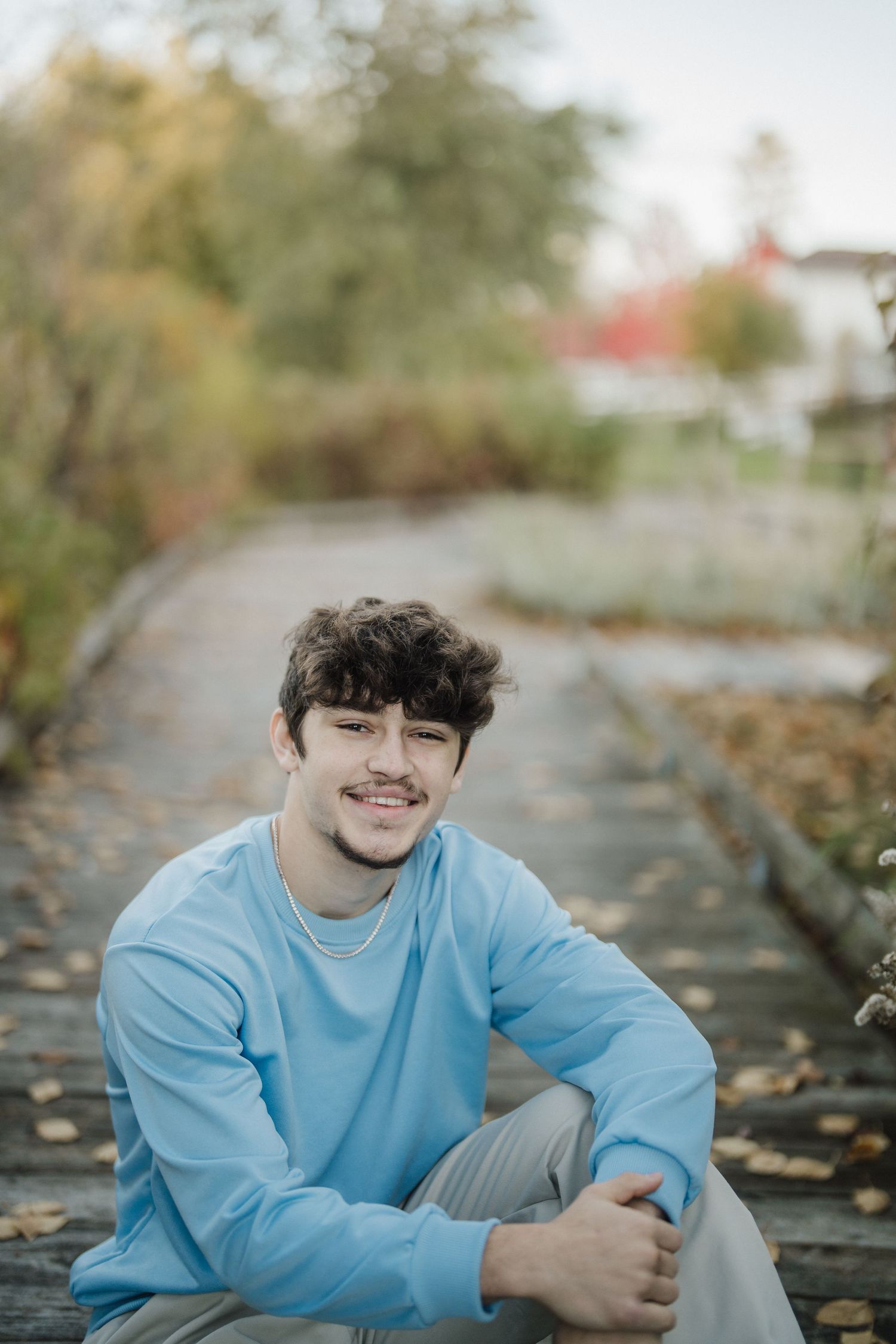 Person in blue sweatshirt sitting on leaf-covered path during fall season.