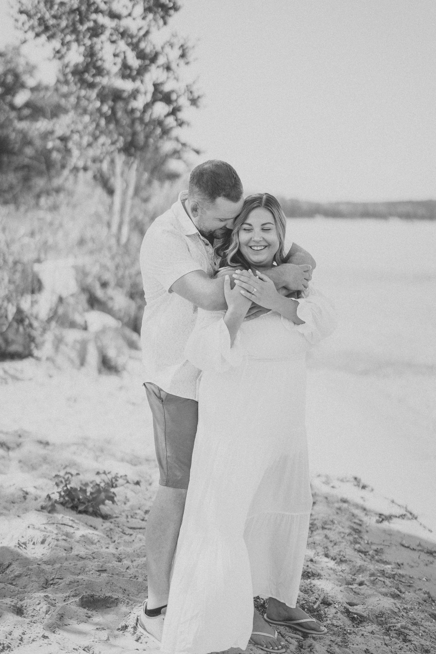 A couple shares joyful candid moments in black and white photos by the water's edge.