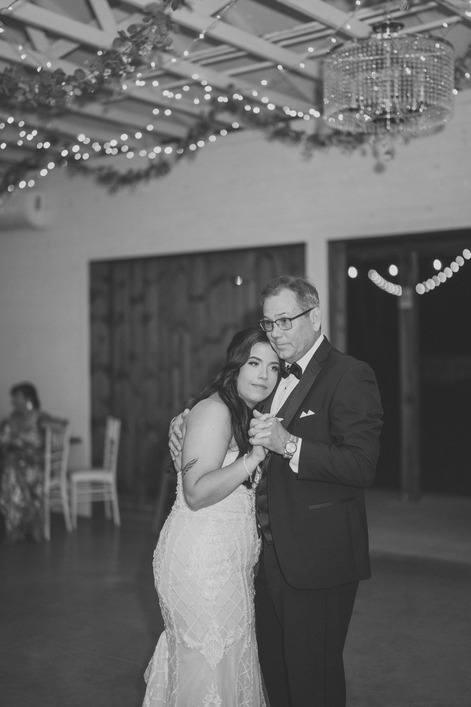 A romantic black and white wedding dance moment under twinkling string lights in an elegant reception venue.