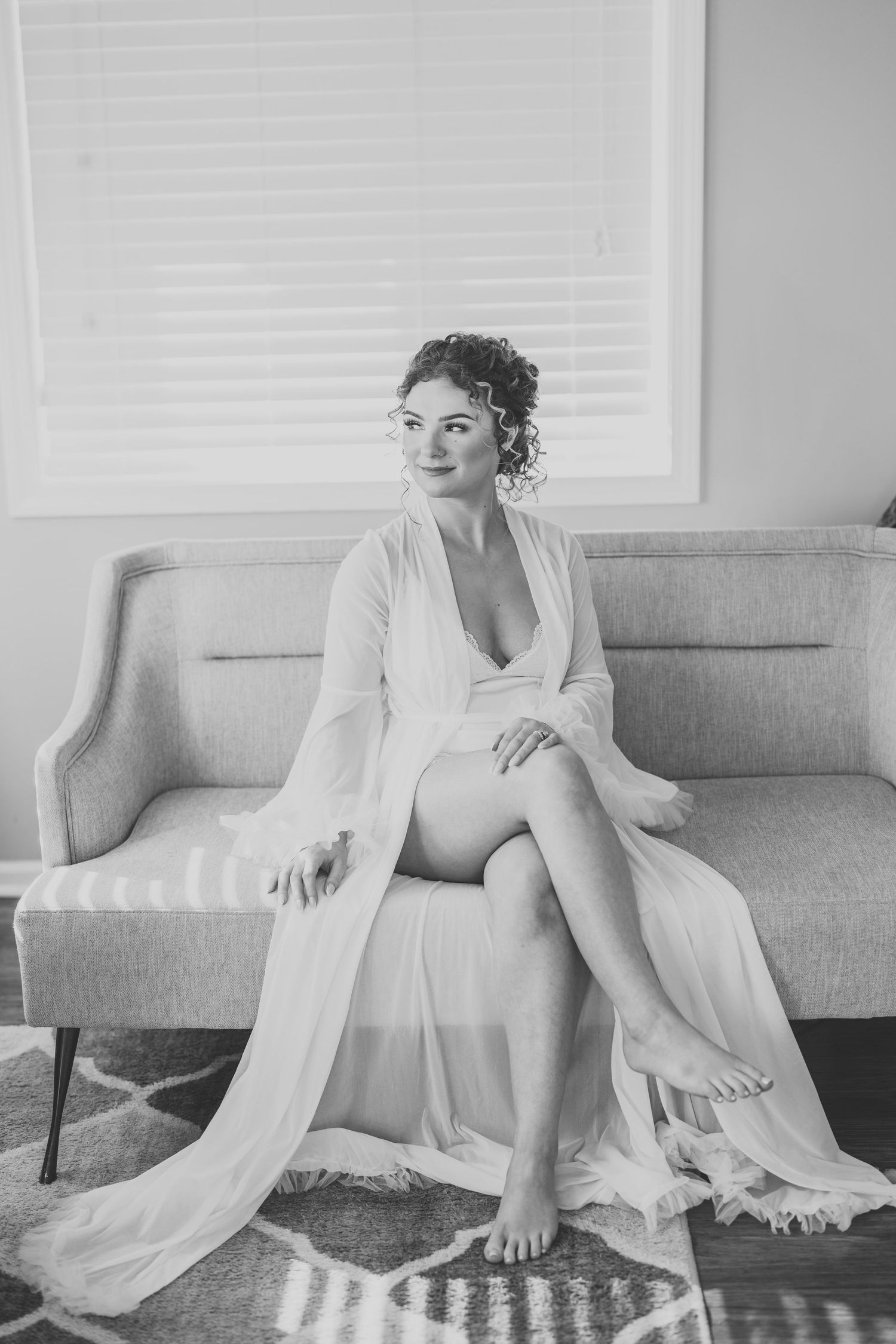 Black and white portrait of person in white robe seated elegantly on gray couch.