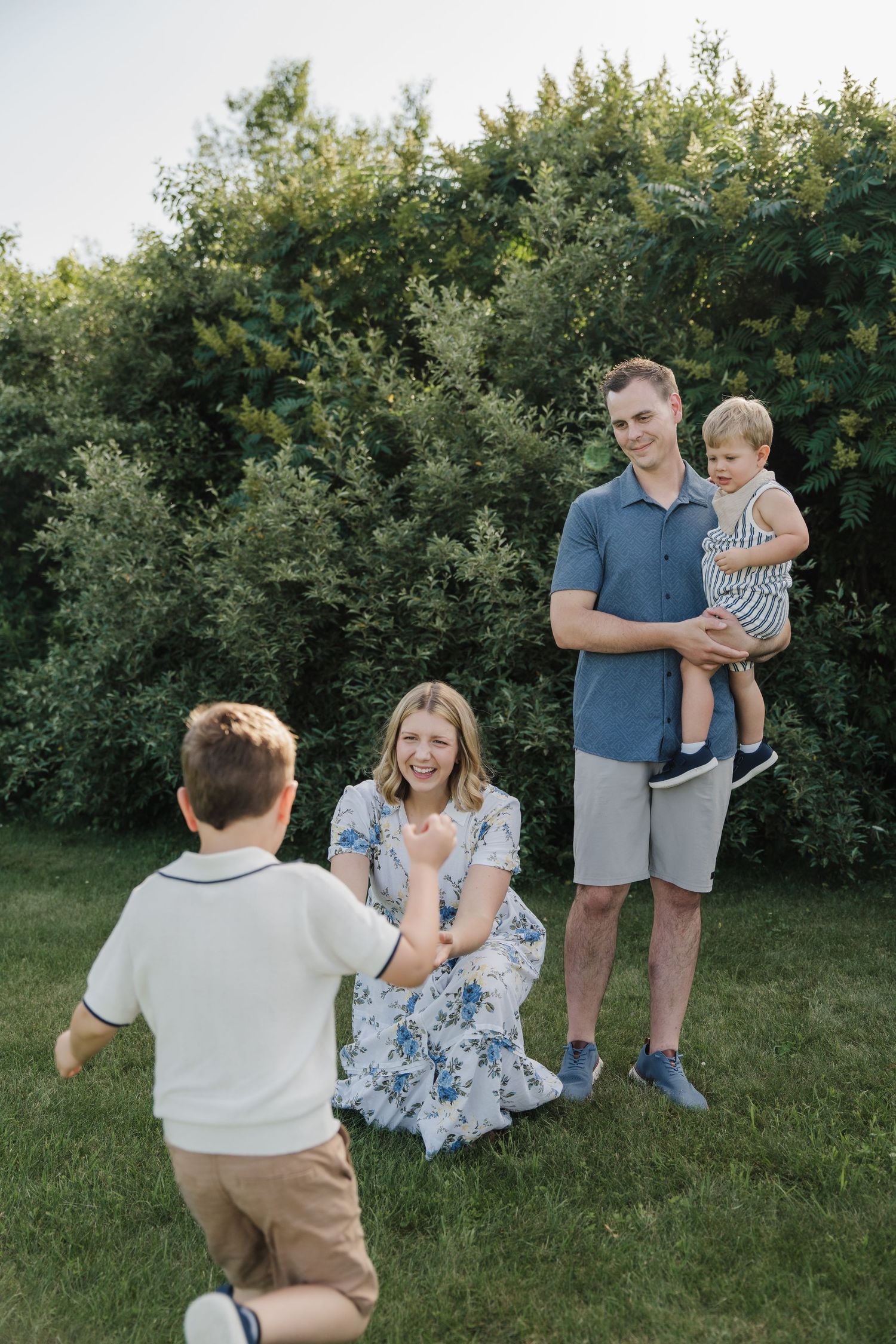 A happy family of four enjoying outdoor time together on a green lawn with lush bushes in the background.