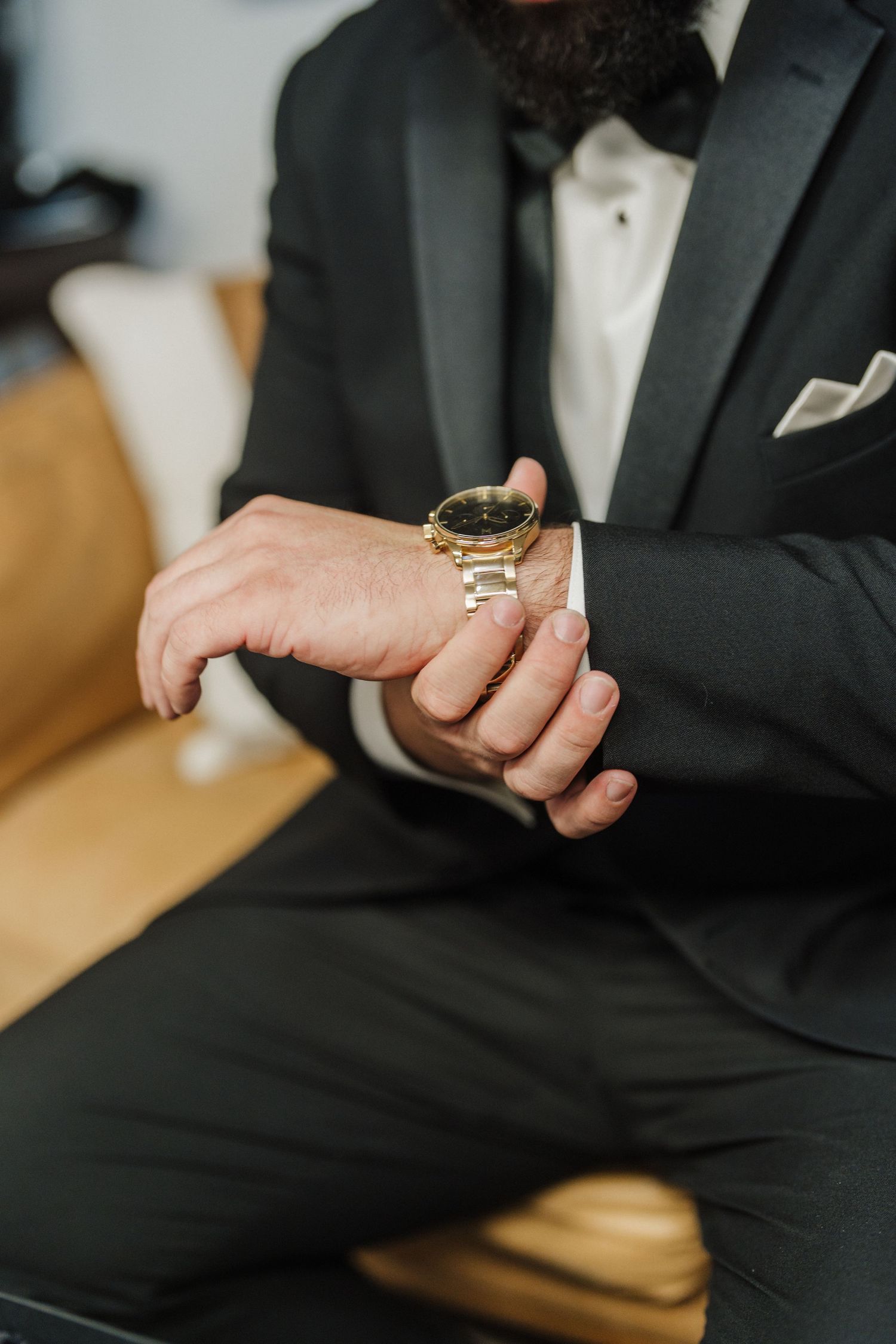 Close-up view of hands wearing a black suit sleeve and gold ring against a light background.