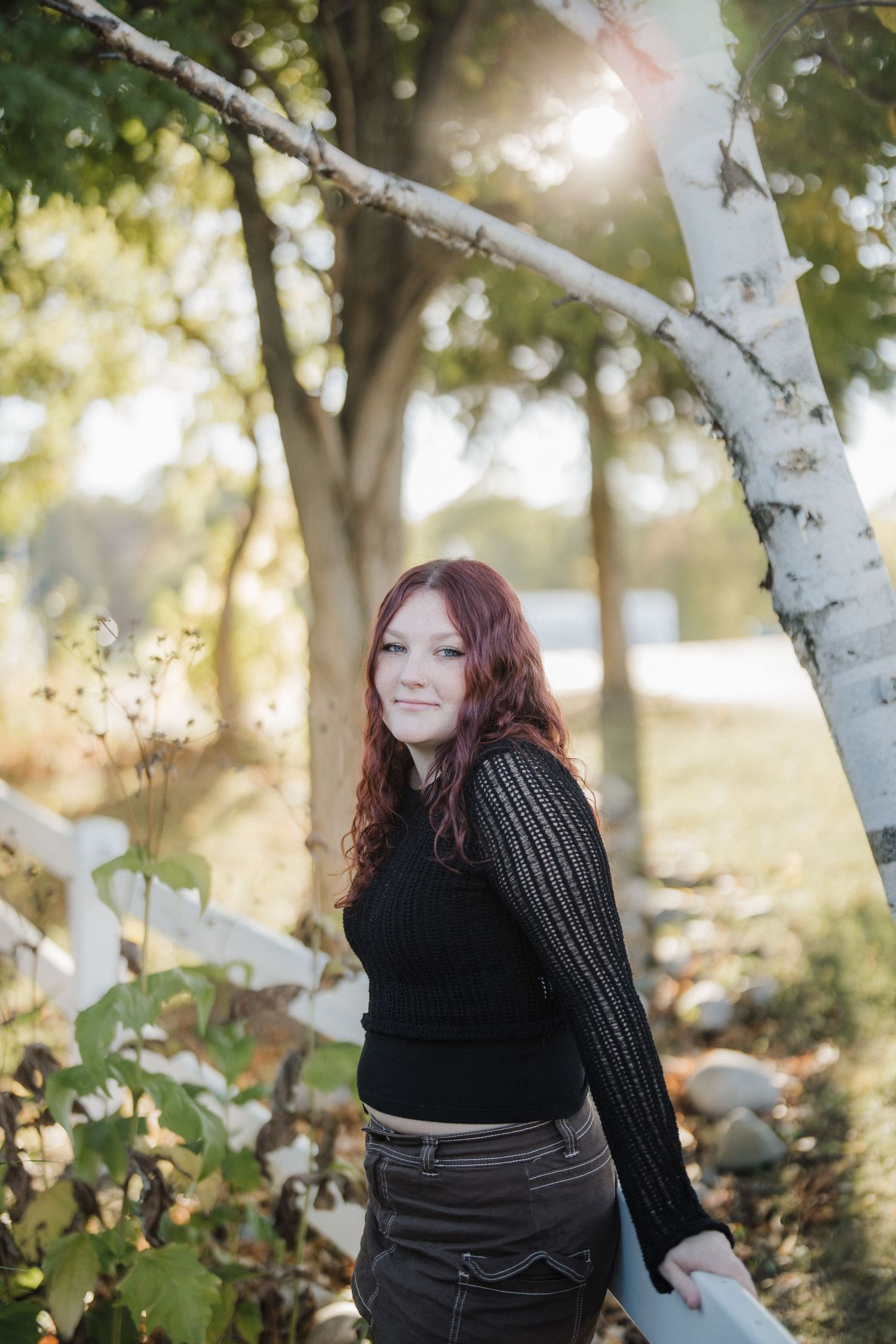 Outdoor portrait in autumn sunlight by white birch tree wearing black sweater and dark pants.