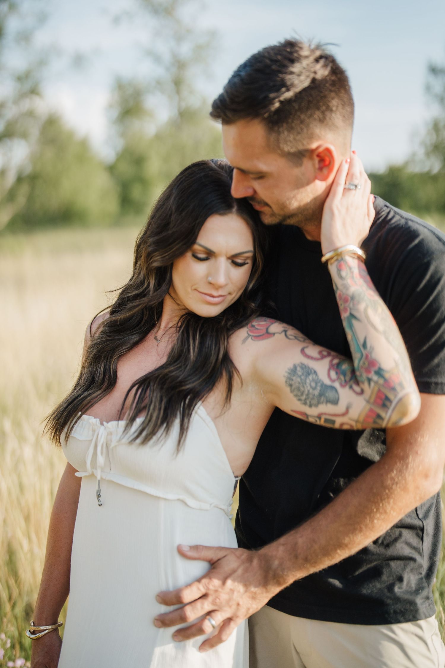 Romantic couple embraces in a sunlit meadow with tall grass during an intimate outdoor photo session.