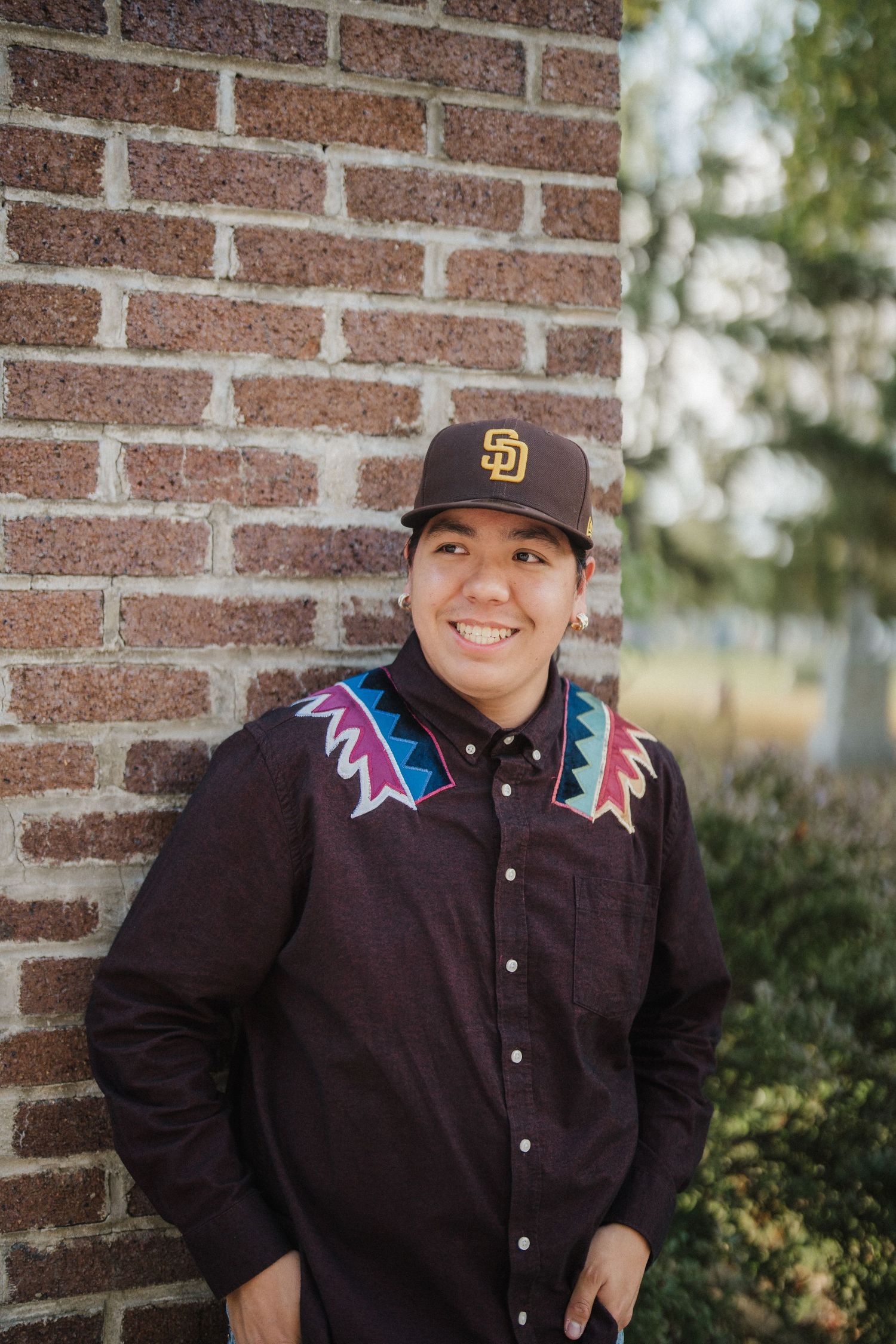 Three casual portraits against a brick wall show someone wearing a San Diego Padres baseball cap and dark button-up shirt.