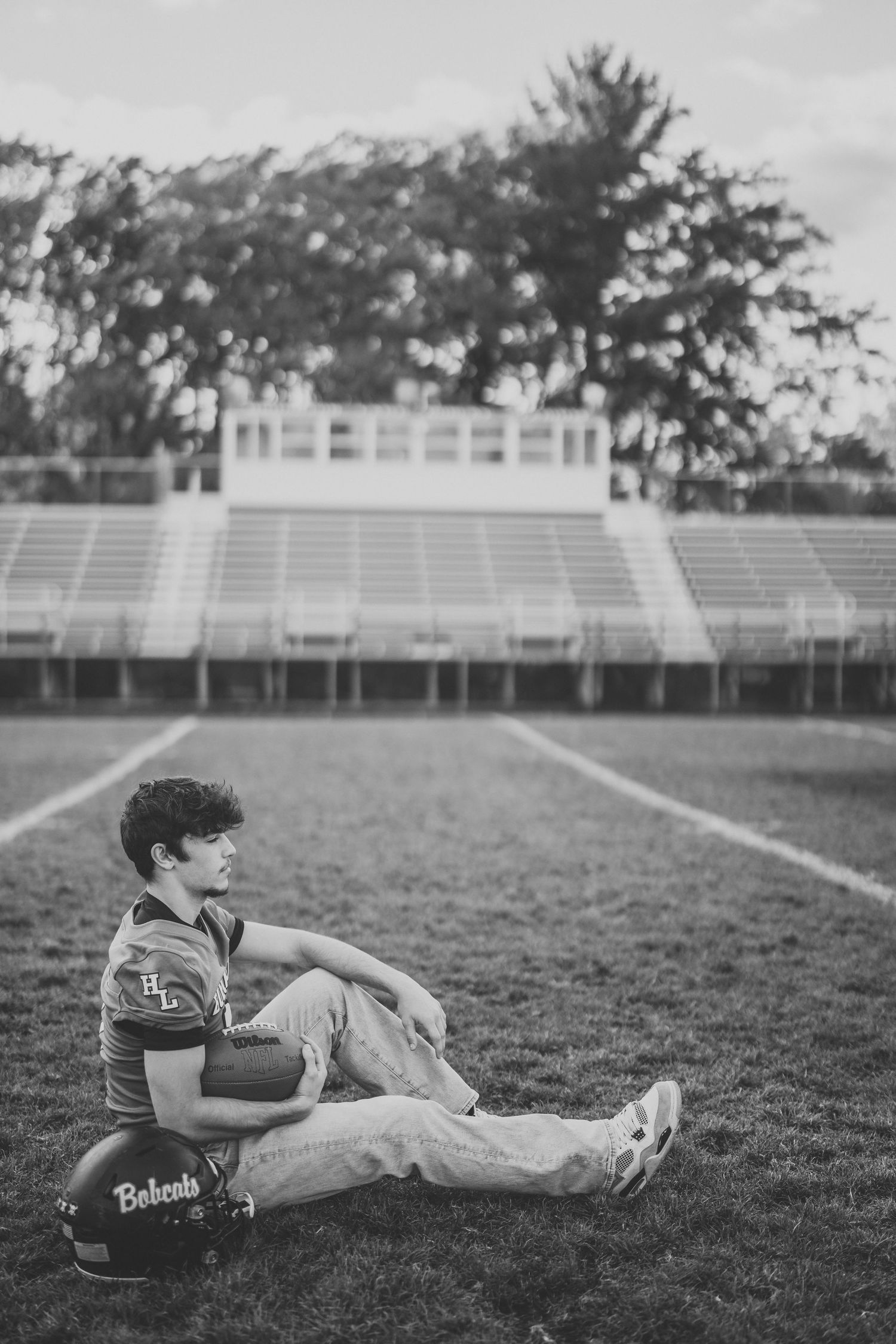 Black and white photo showing someone laying on a football field with stadium bleachers in the background.