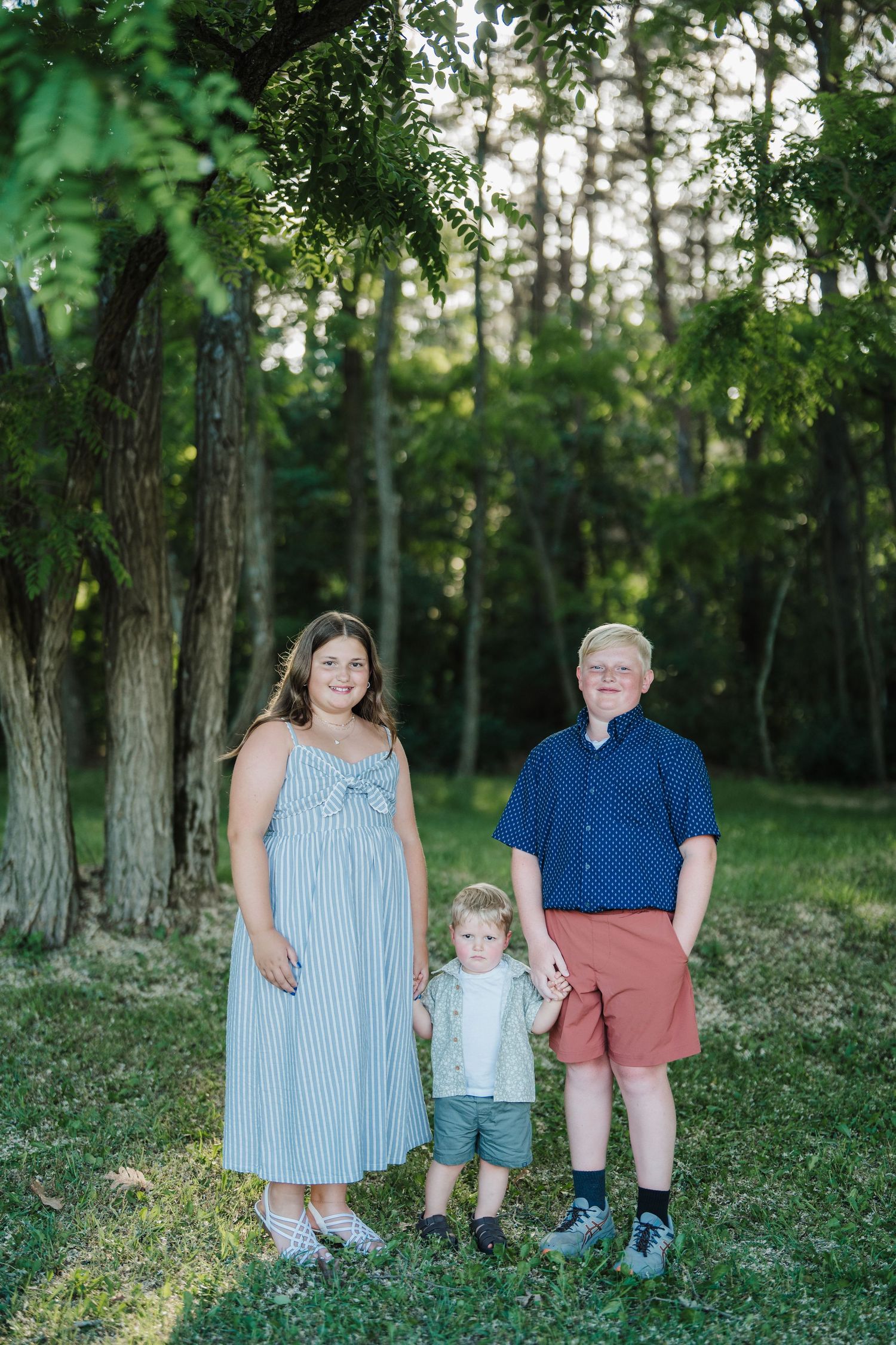 A family poses together outdoors in a wooded area during a summer photo session.