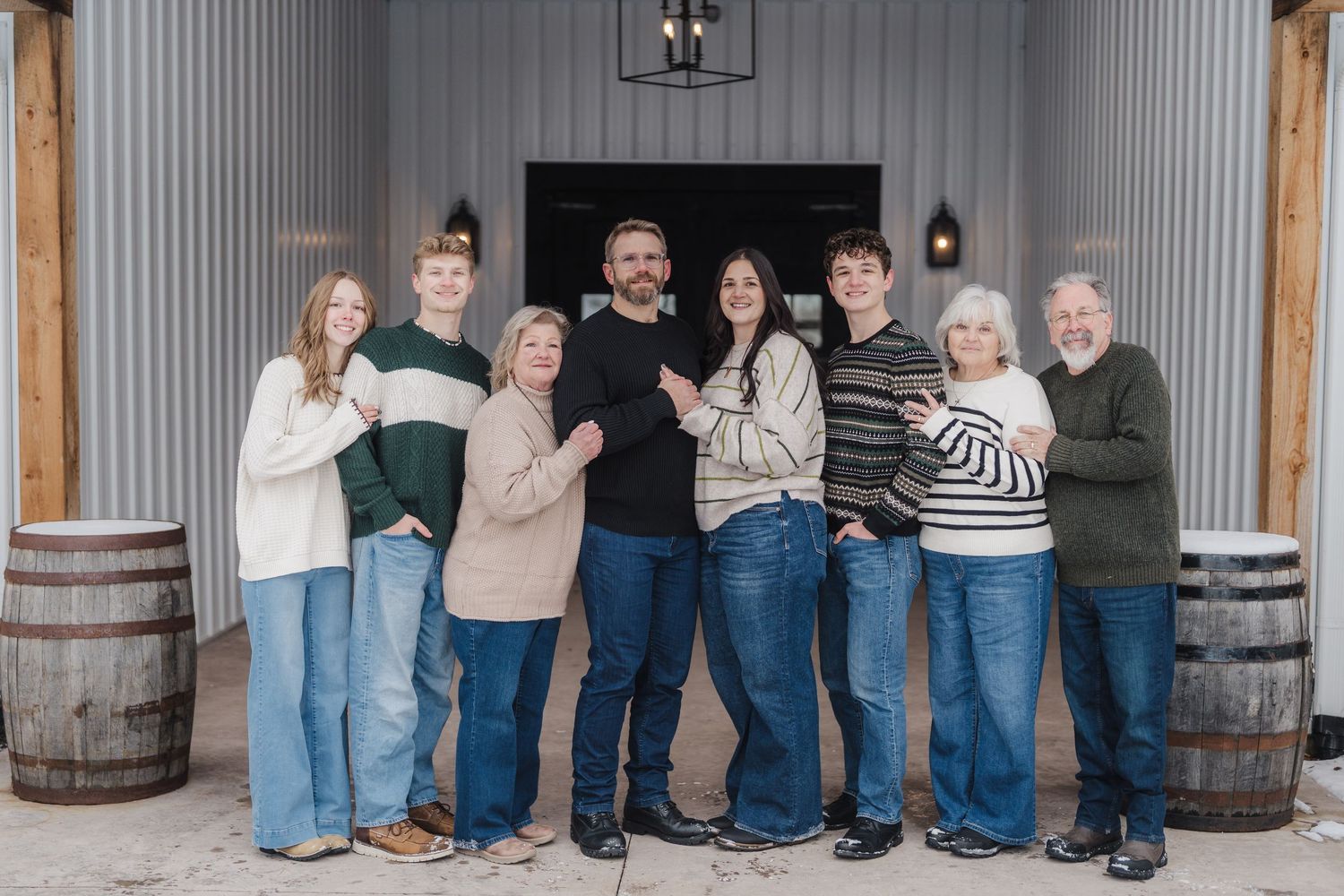 A group poses together inside a rustic barn or warehouse with metal walls and wooden barrels.
