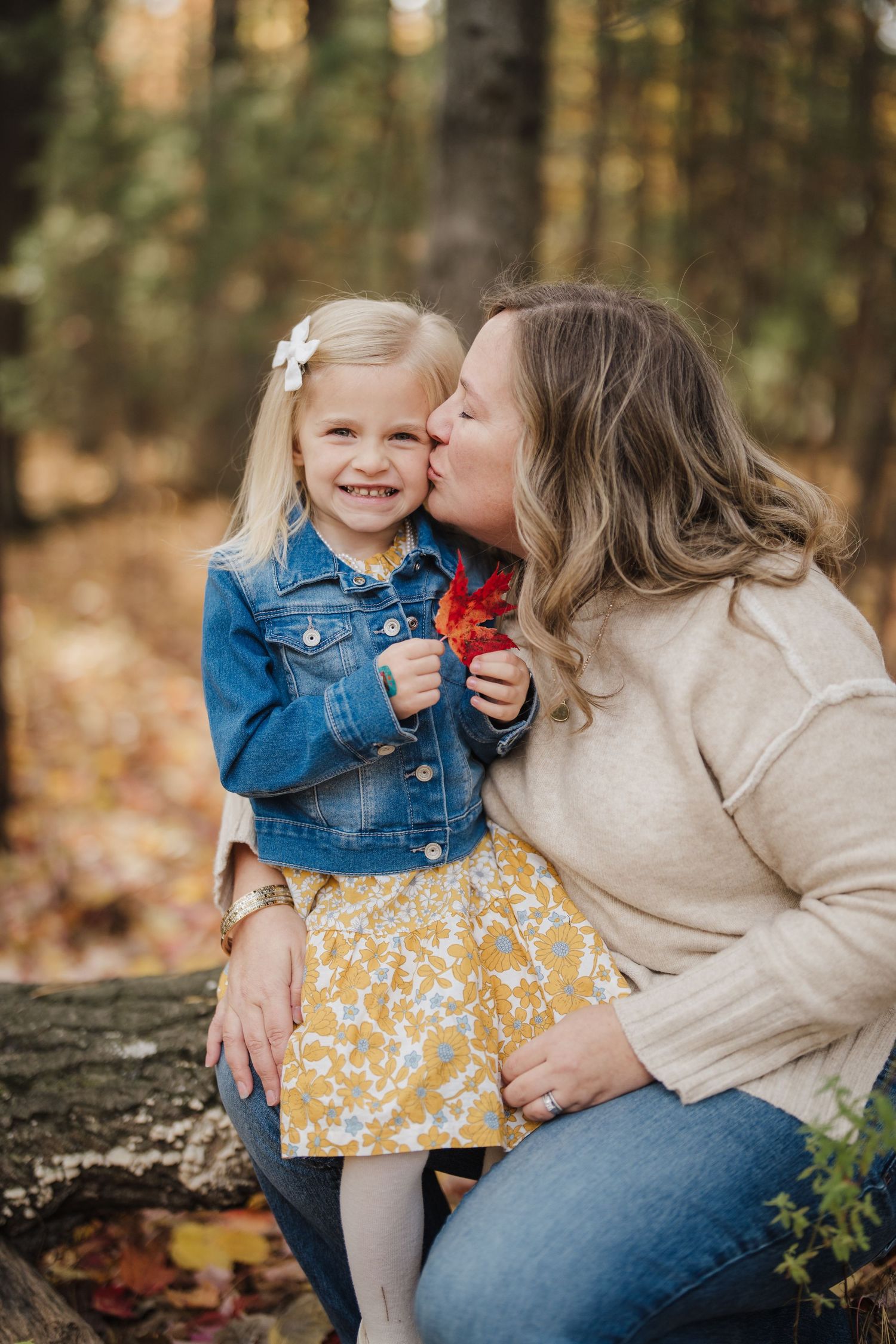 A sweet autumn photoshoot in the woods shows tender moments between parent and child in denim and yellow floral dress.