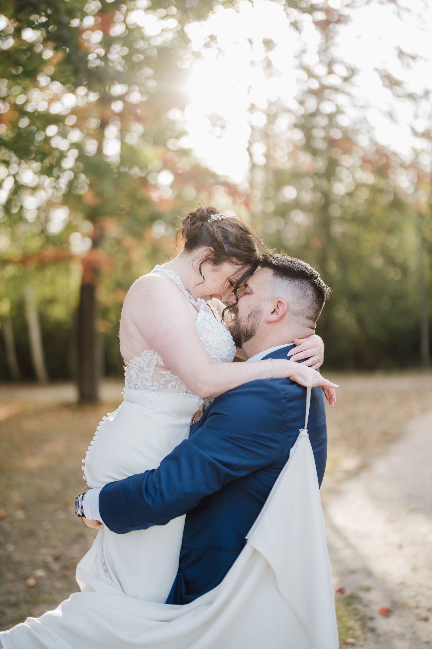 An intimate wedding moment captured on a wooded path with the couple embracing.