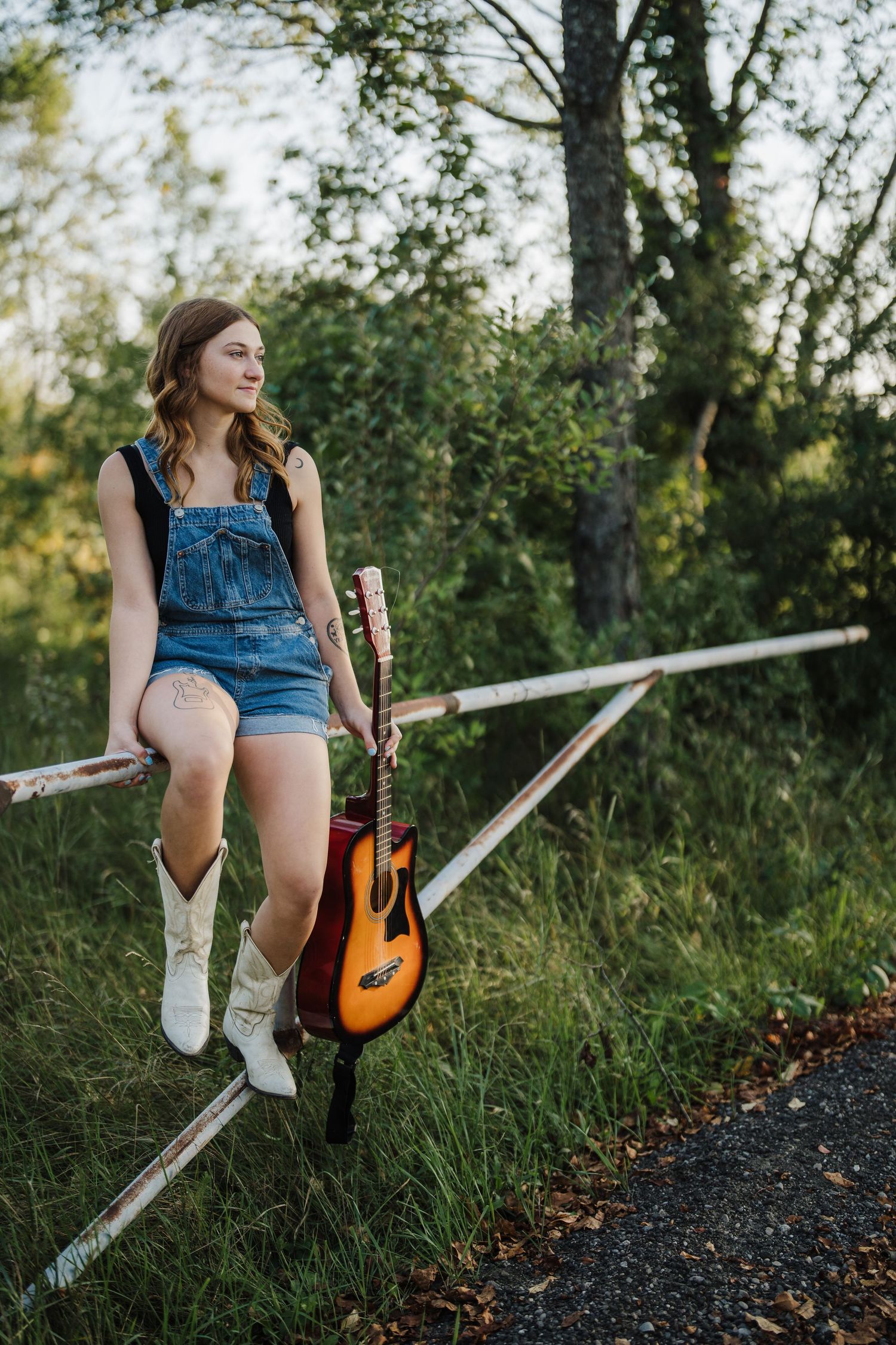 A casual portrait session with guitar along a rural path featuring denim and boots styling.