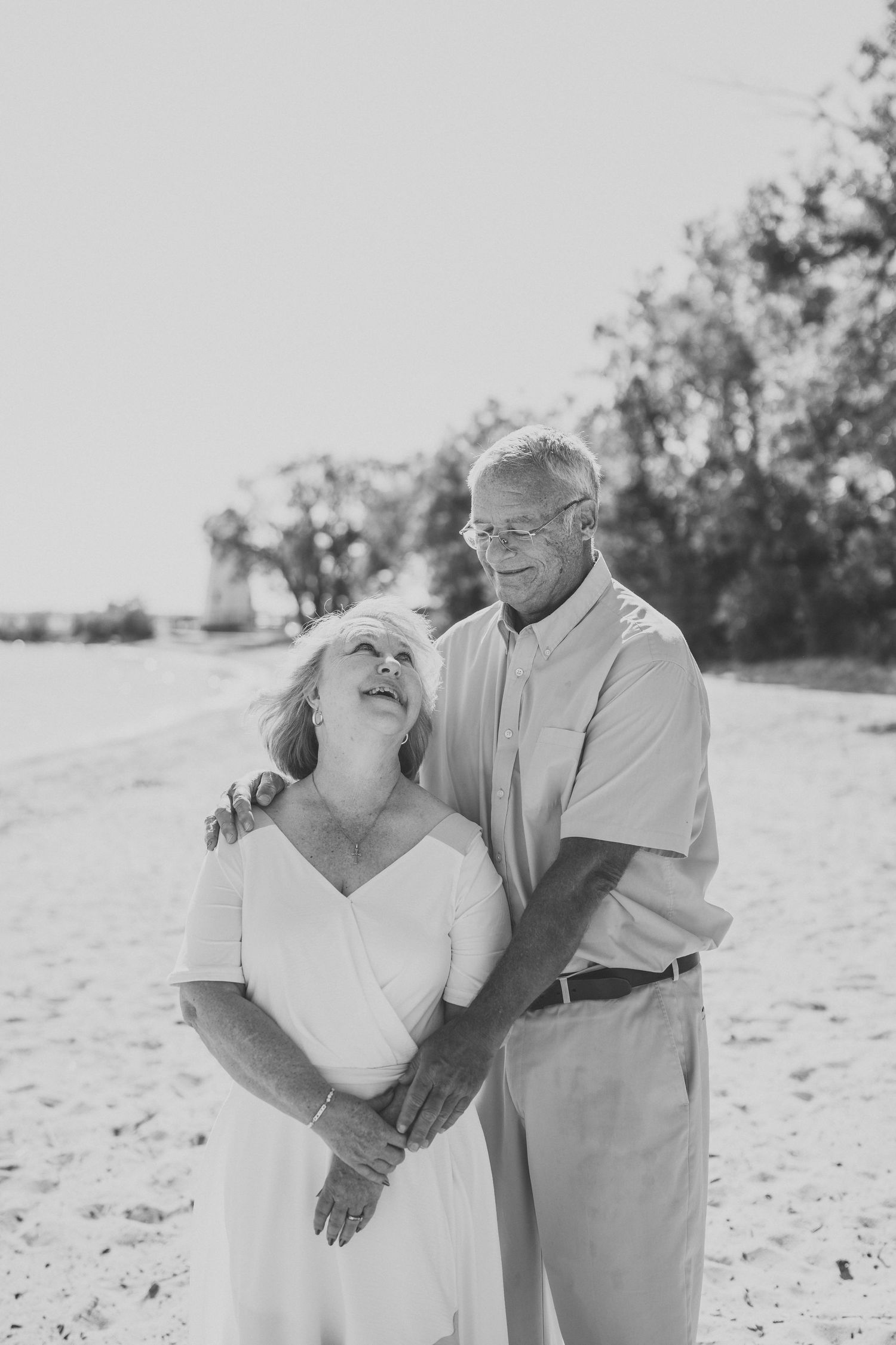 Elderly couple embracing and laughing together on a sunny beach in black and white photography.