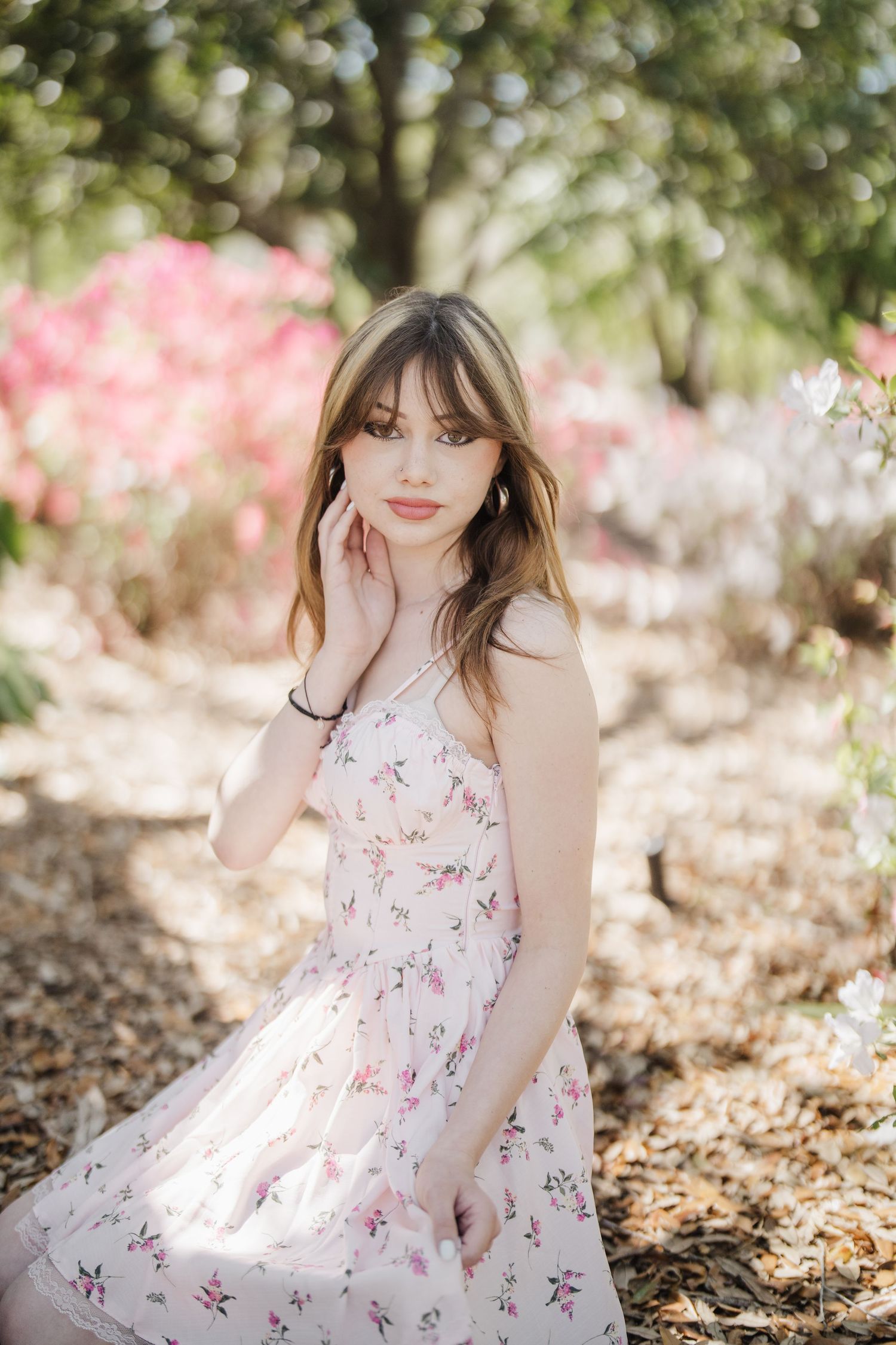 A light pink floral dress flows gracefully in a sunlit garden with blooming flowers in the background.