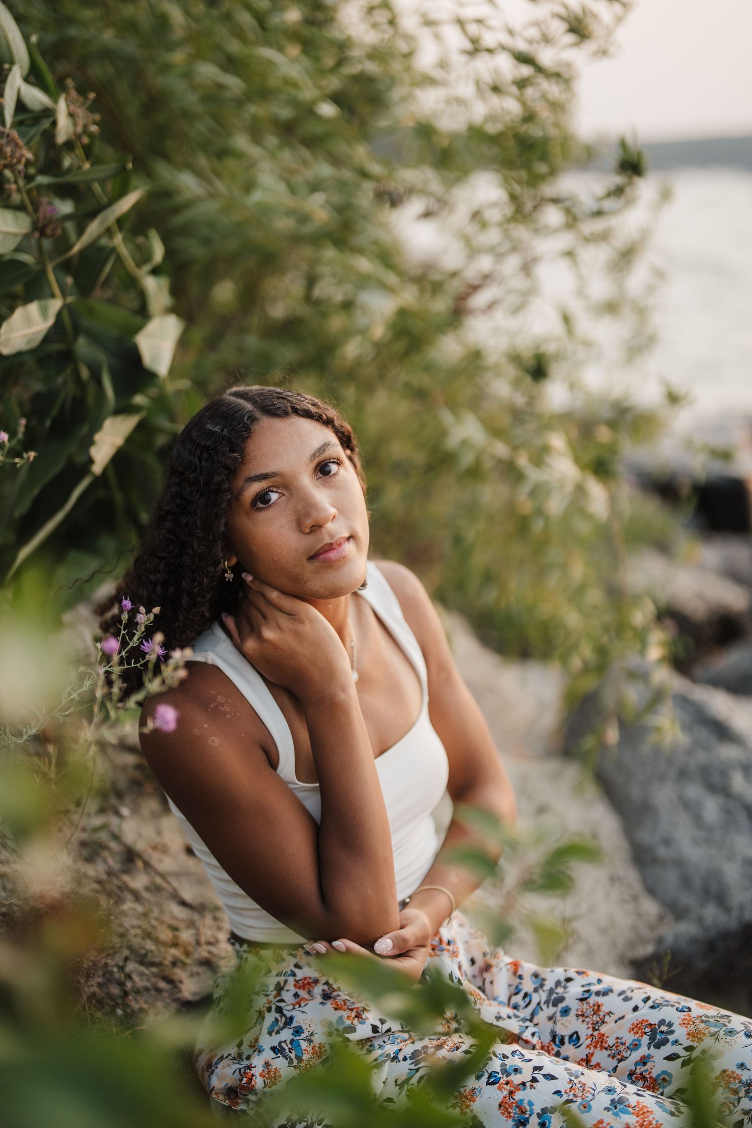 Artistic outdoor portrait among greenery and rocks featuring a white top and floral dress.