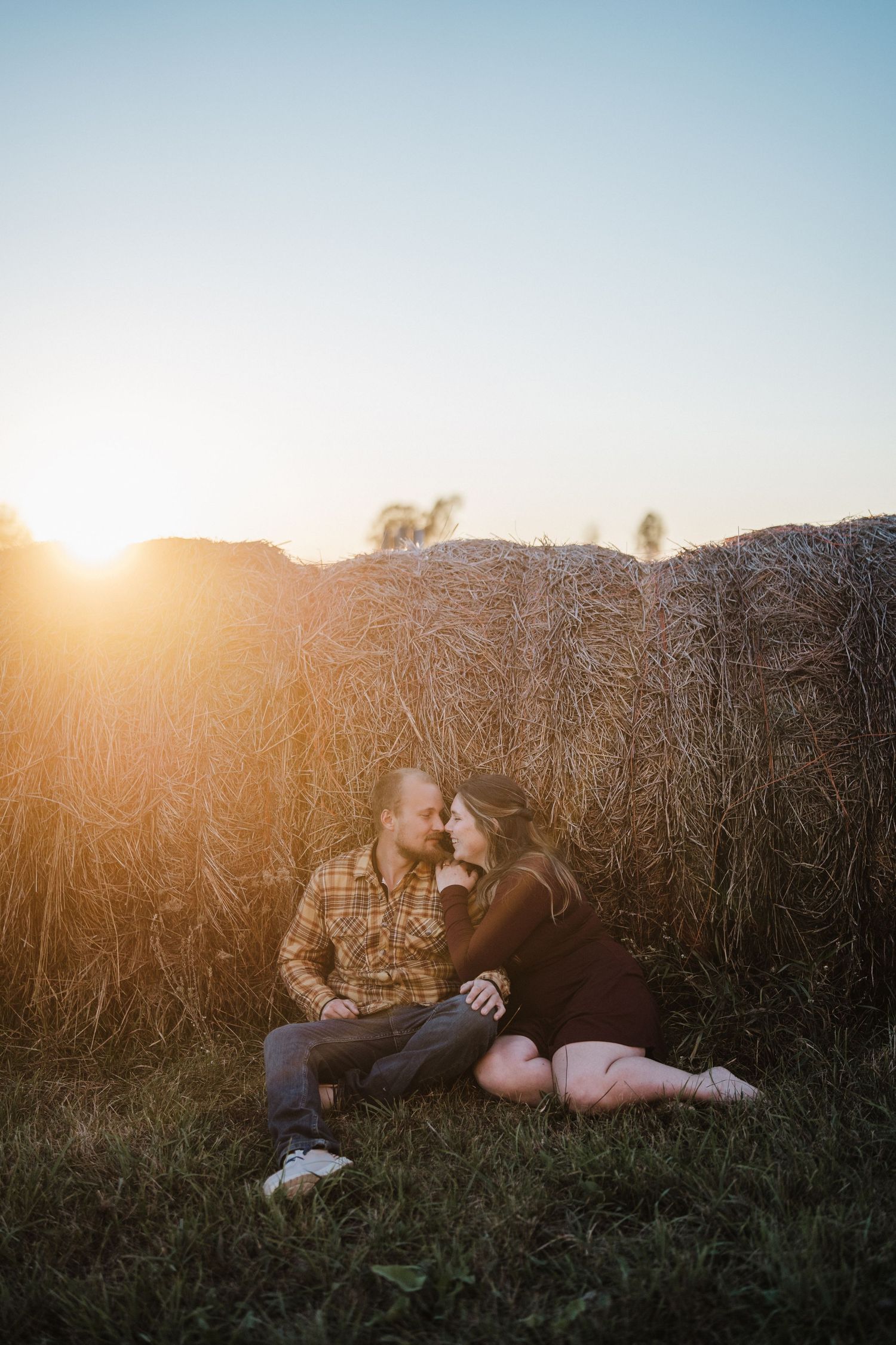 Silhouettes of couple relaxing in tall grass field during golden sunset hour.