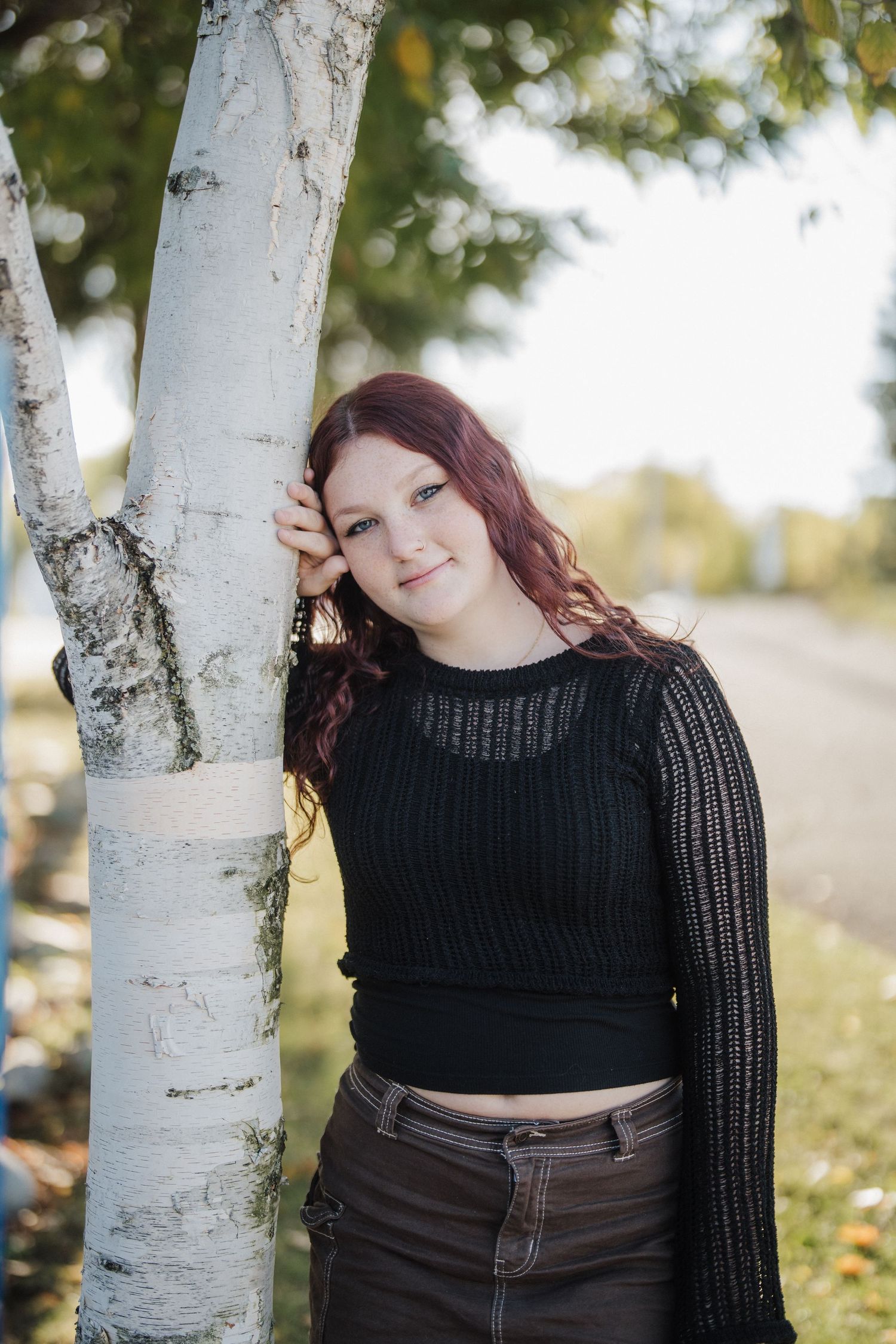 A person in a black sweater poses against white birch trees in an outdoor setting.