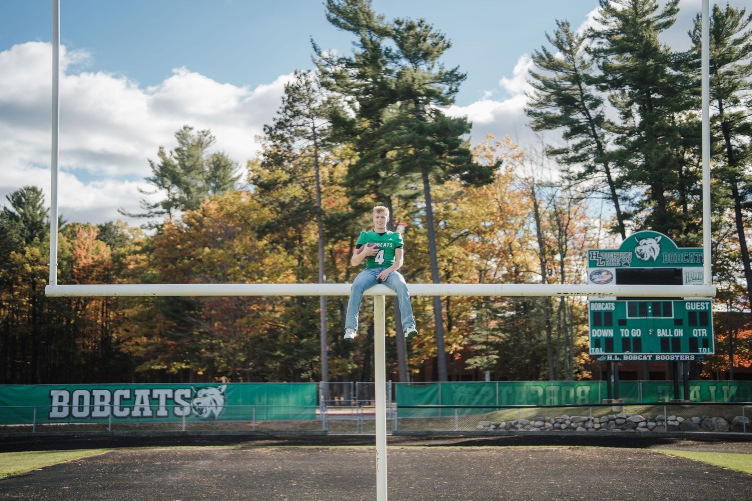 Football goalpost at Bobcats field with tall pine trees and autumn foliage in background.