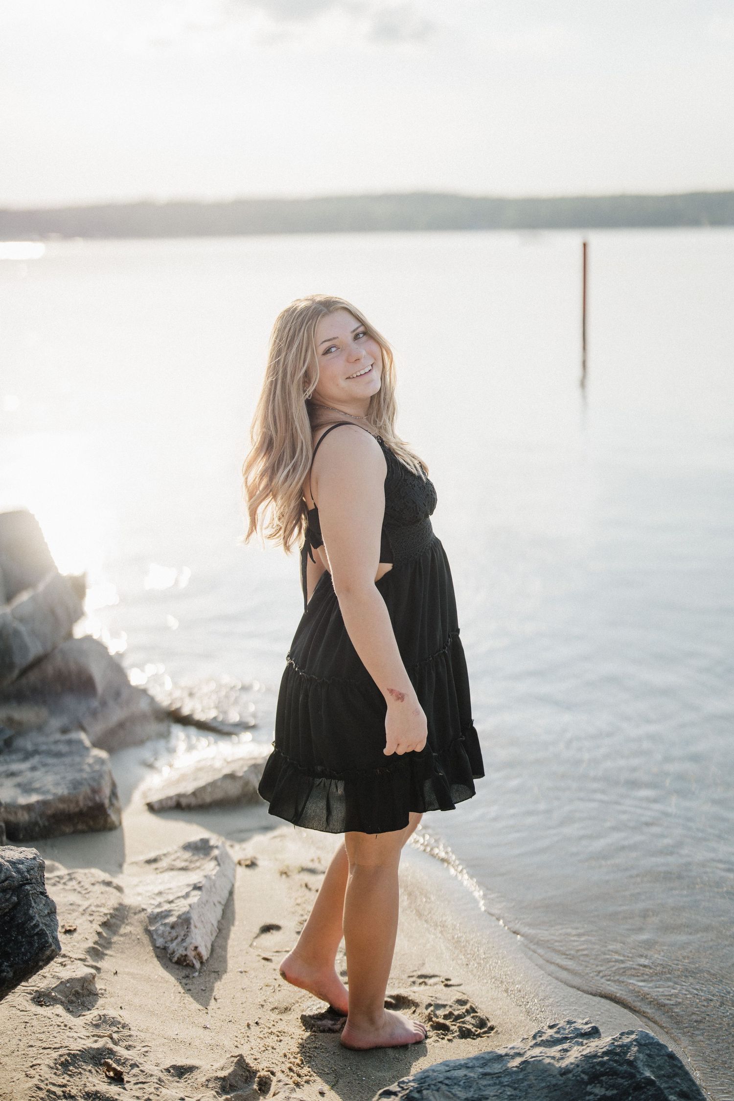 A person in a black dress poses by the water's edge at sunset creating silhouettes against the shimmering lake.