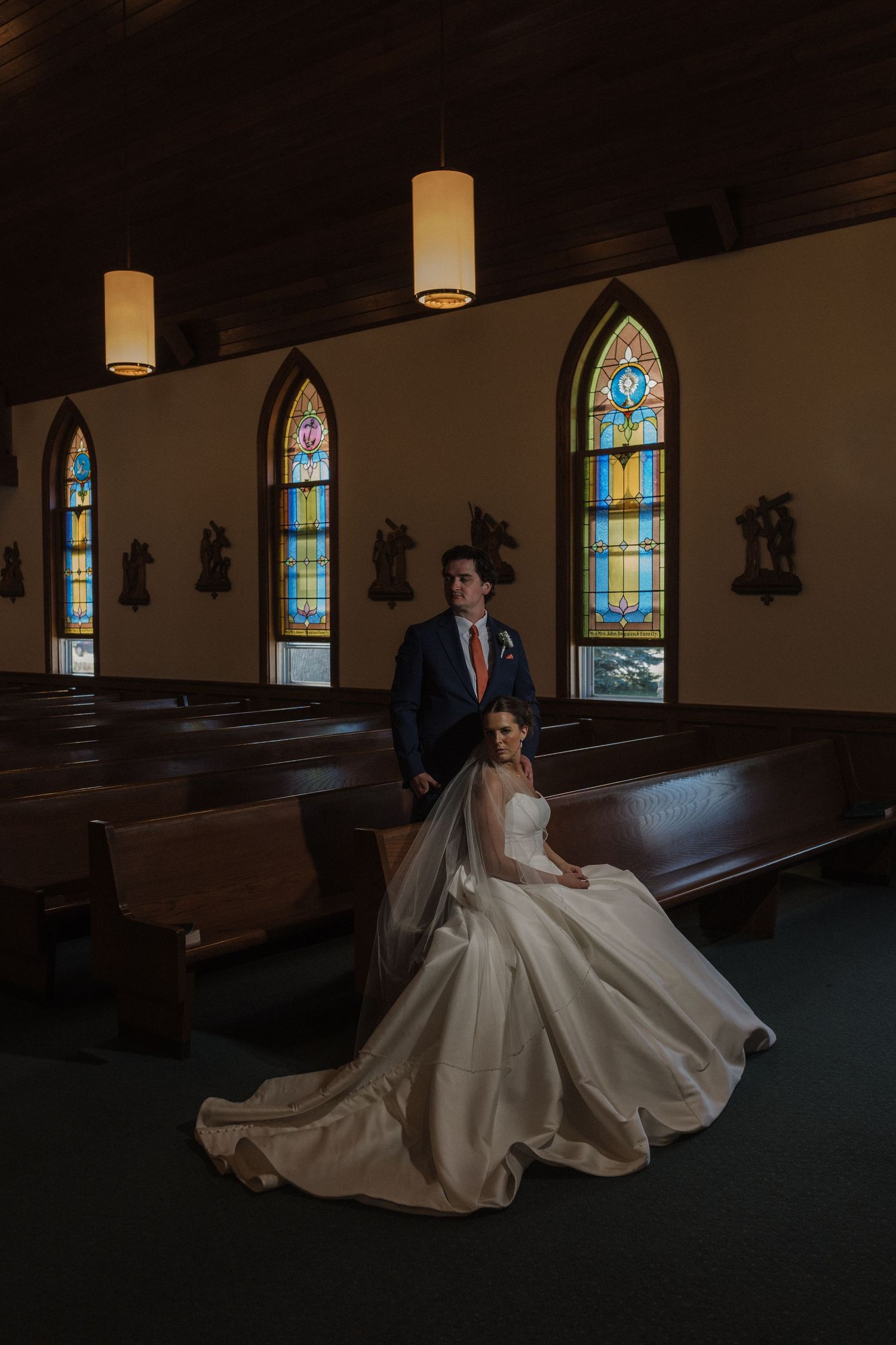 Dramatic wedding photo in dark church with stained glass windows and flowing white gown.