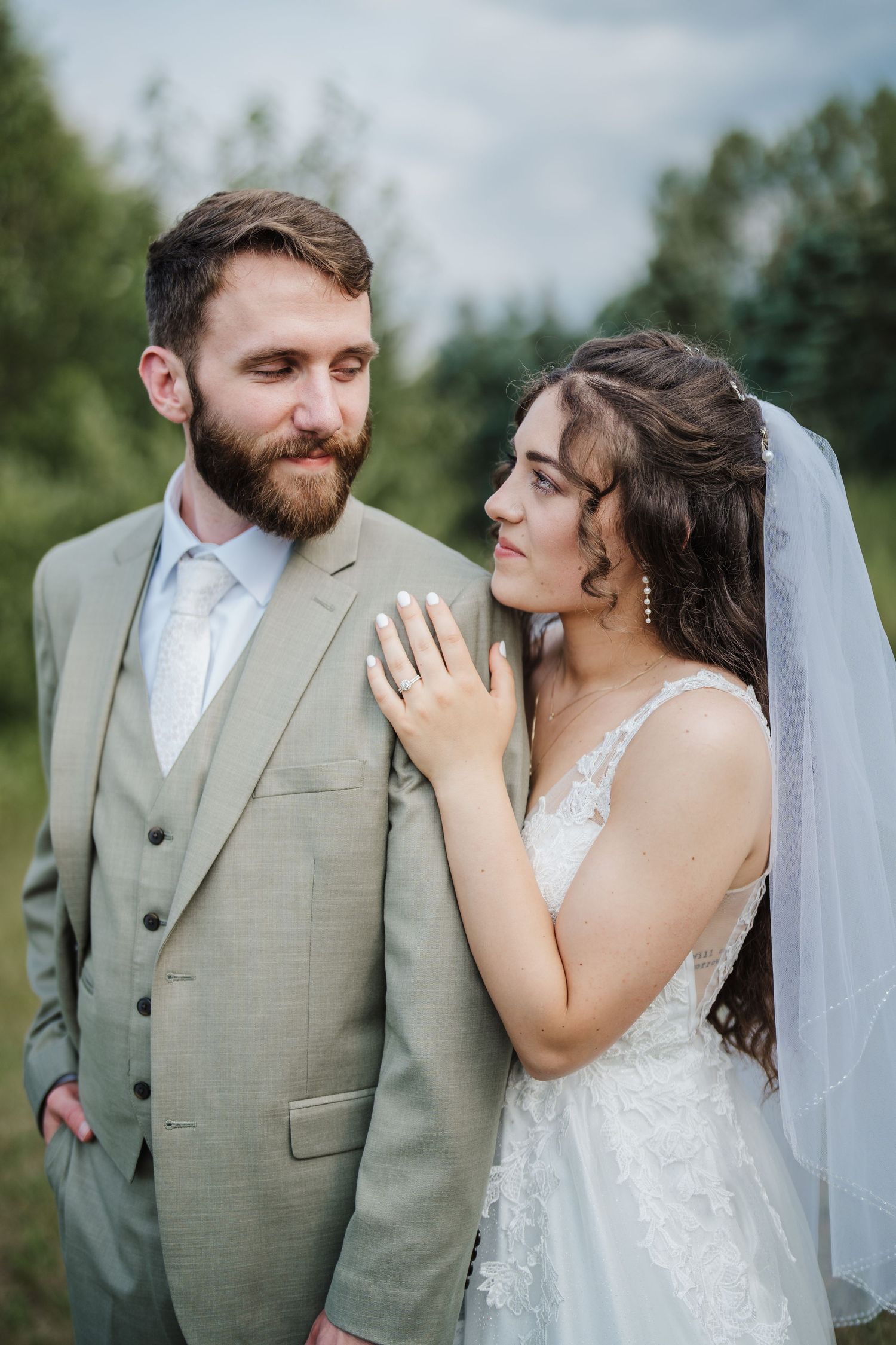A romantic wedding portrait shows the couple in a light grey suit and lace dress against a nature backdrop.