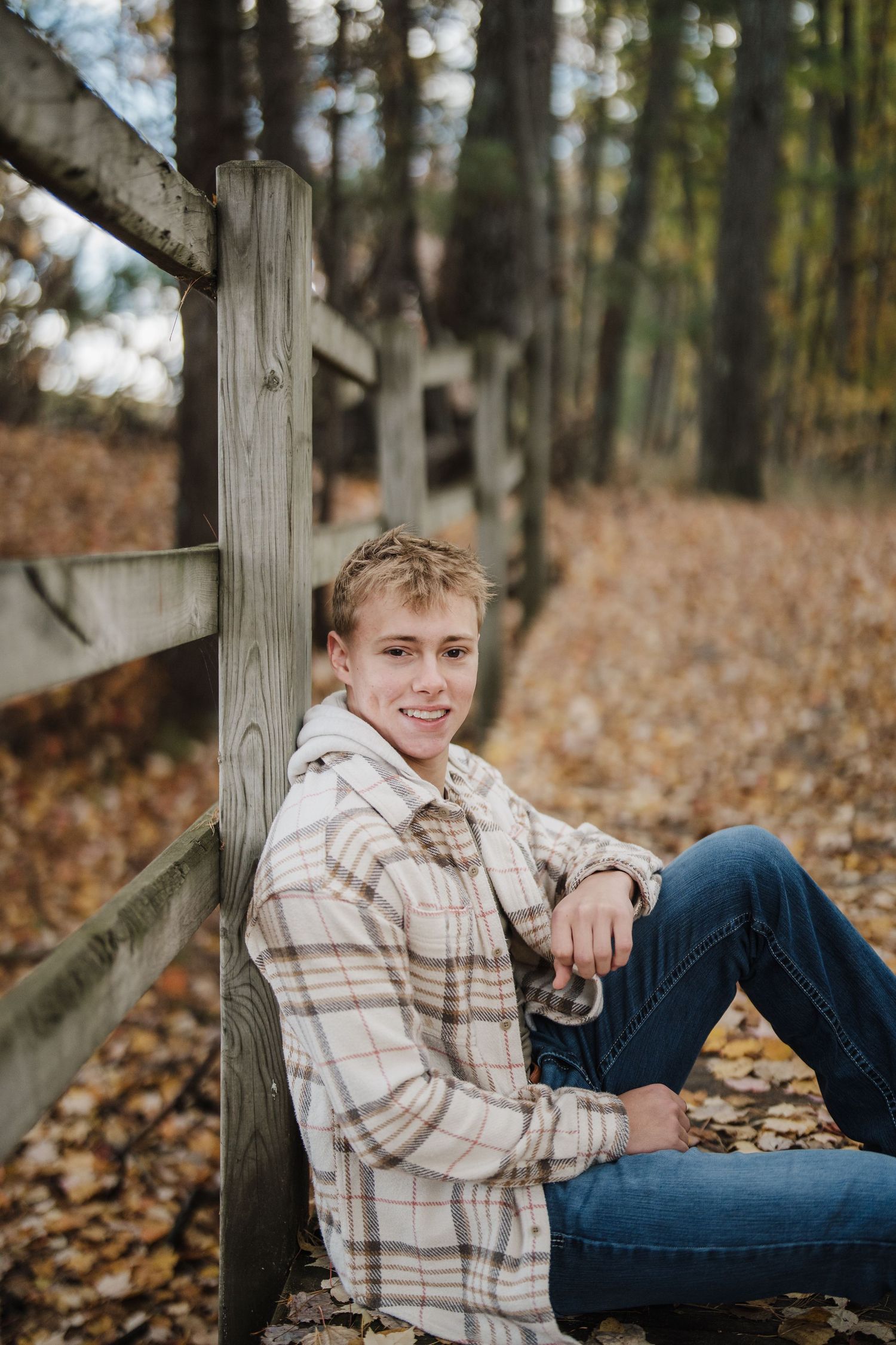 A casual fall portrait session in a wooded area with autumn leaves scattered on the ground.