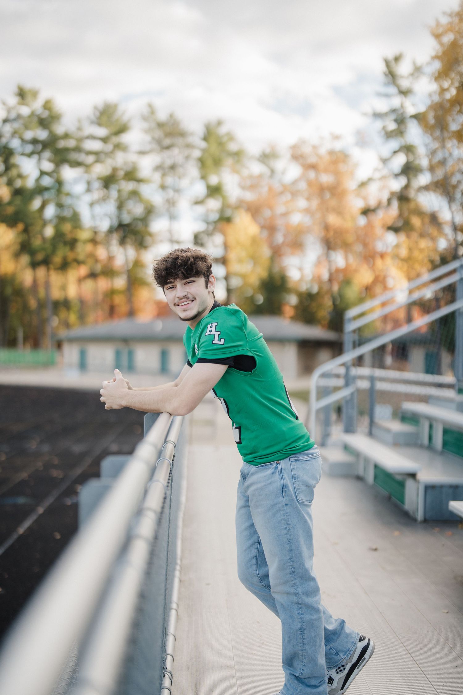 Athletic figure in green jersey and jeans poses on stadium bleachers during golden hour.