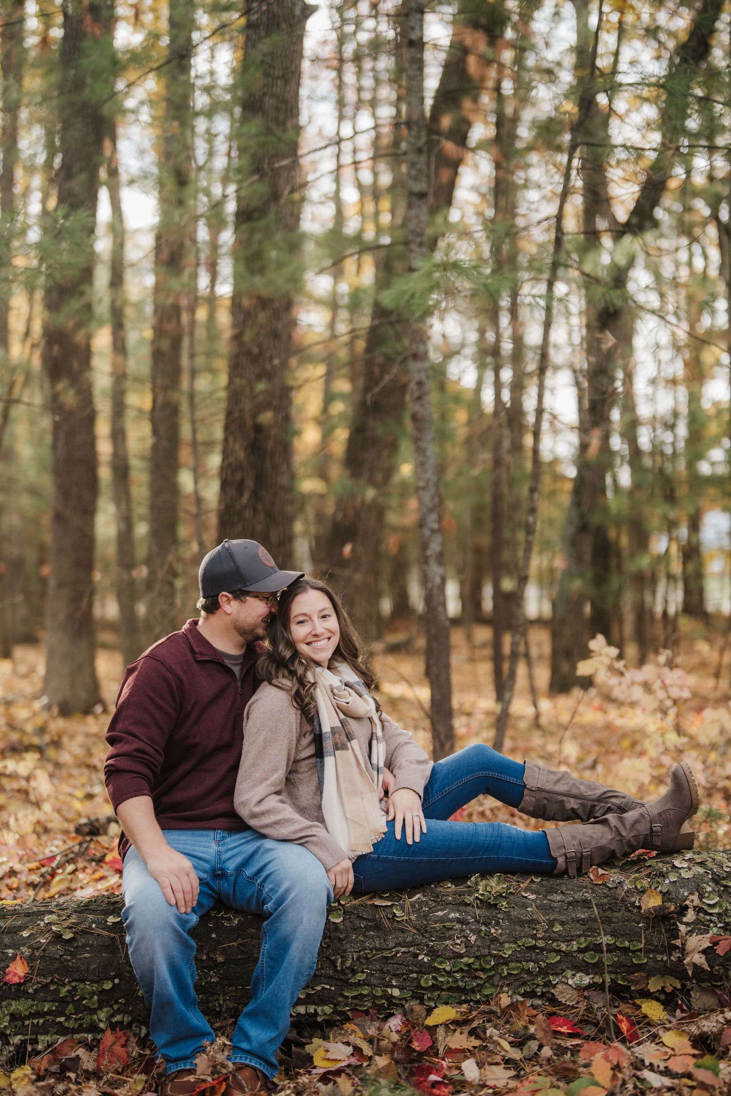 A couple relaxes on a fallen tree trunk in a wooded area during autumn.
