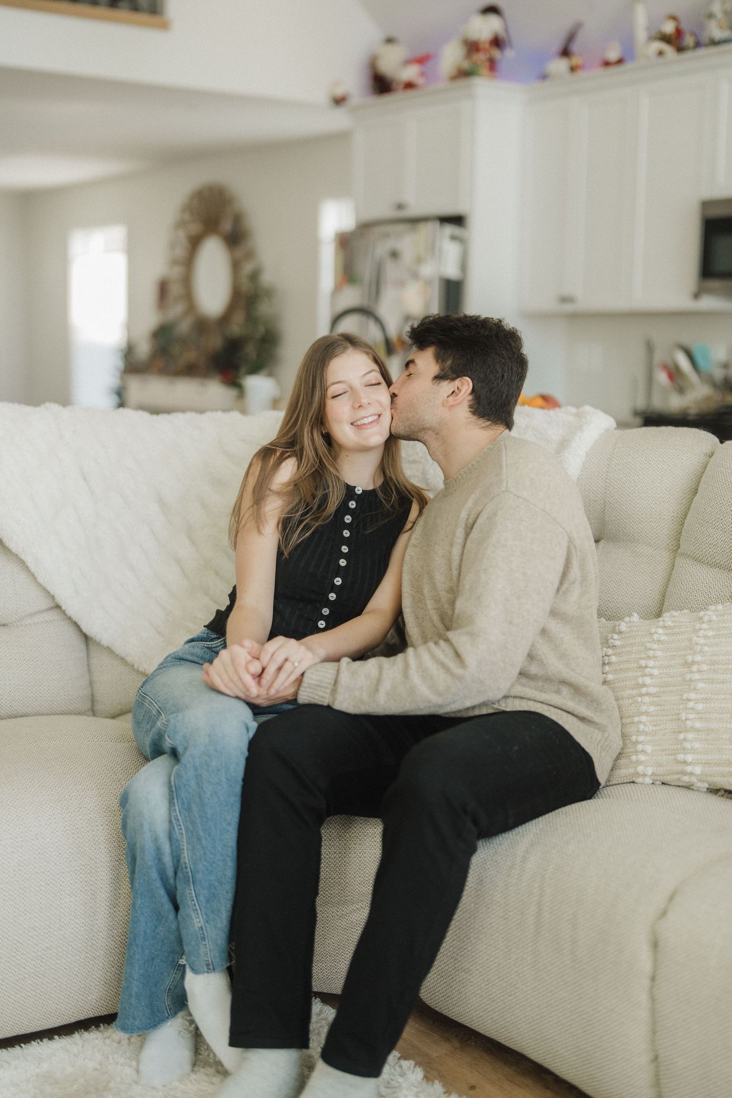 A couple shares tender moments while relaxing together on a white couch in a bright living room.