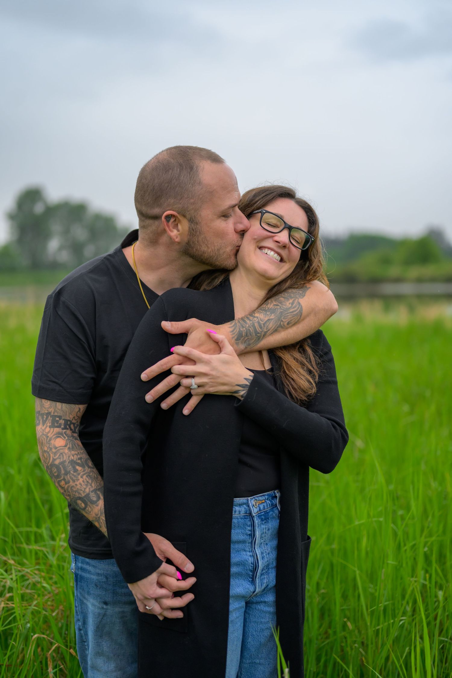 Couple sharing playful moments in a green field on an overcast day.