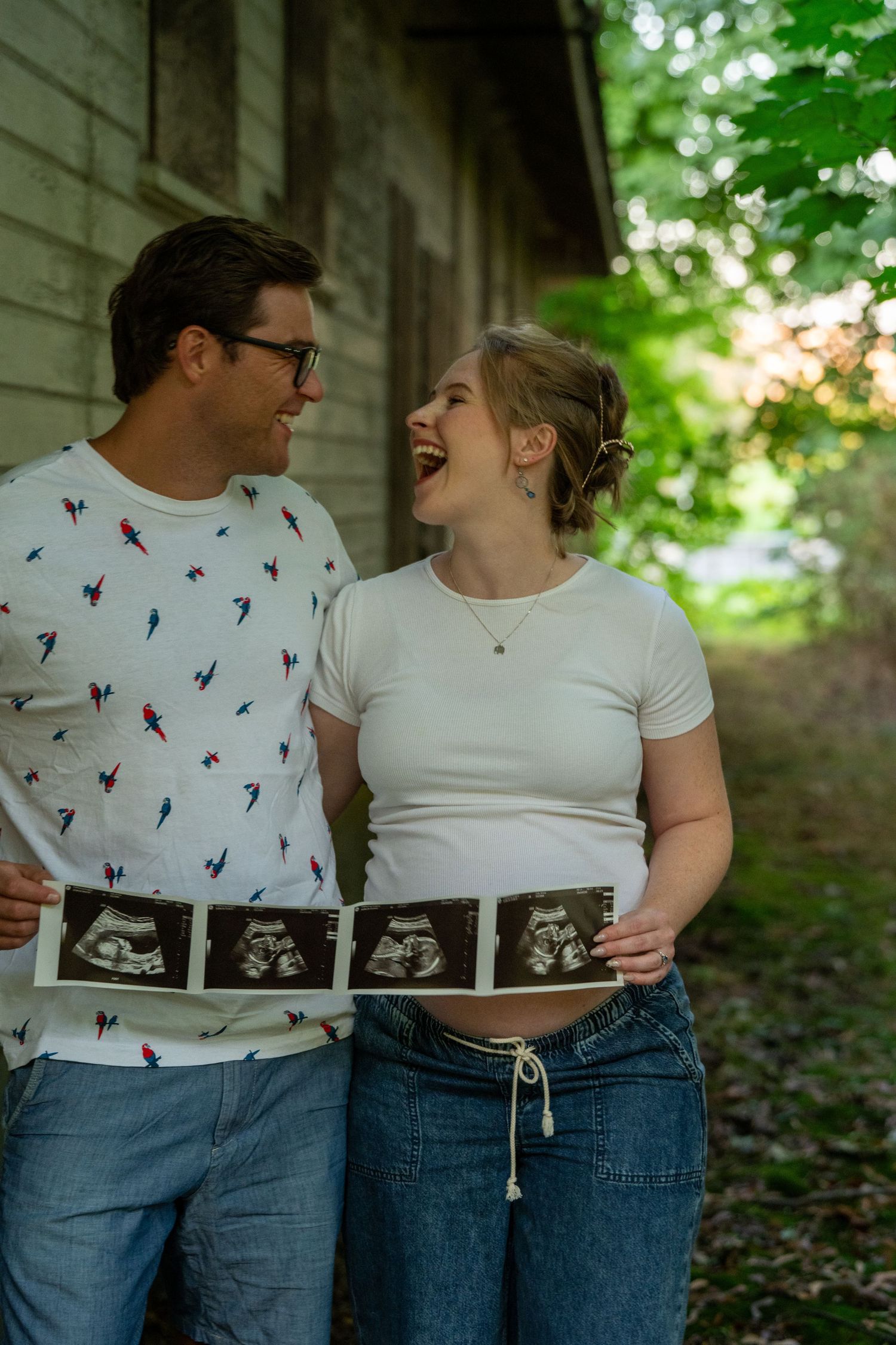 Happy couple laughing together outdoors while holding ultrasound photos, announcing their pregnancy.