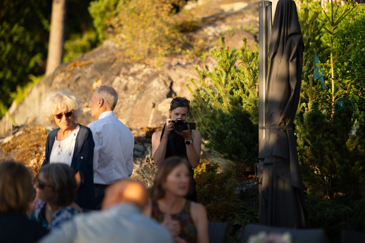 Outdoor gathering of guests mingling during golden hour with trees and natural scenery in the background.