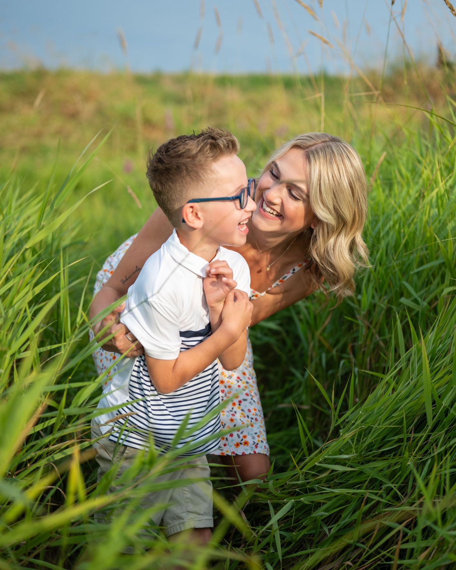 Playful family moment captured in tall green grass during golden hour outdoor photoshoot.