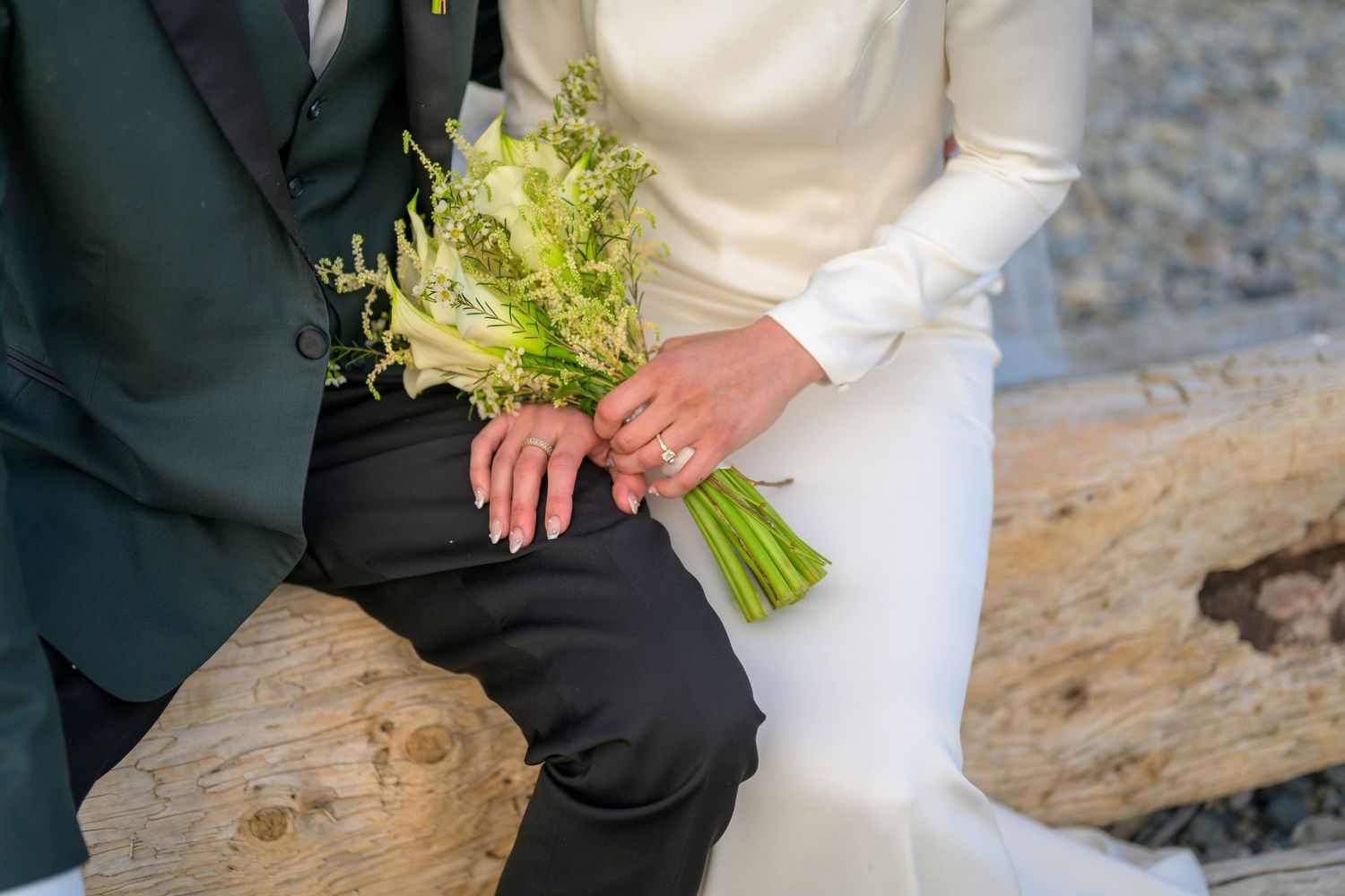 Wedding couple walking hand in hand along a rocky beach with white bouquet.