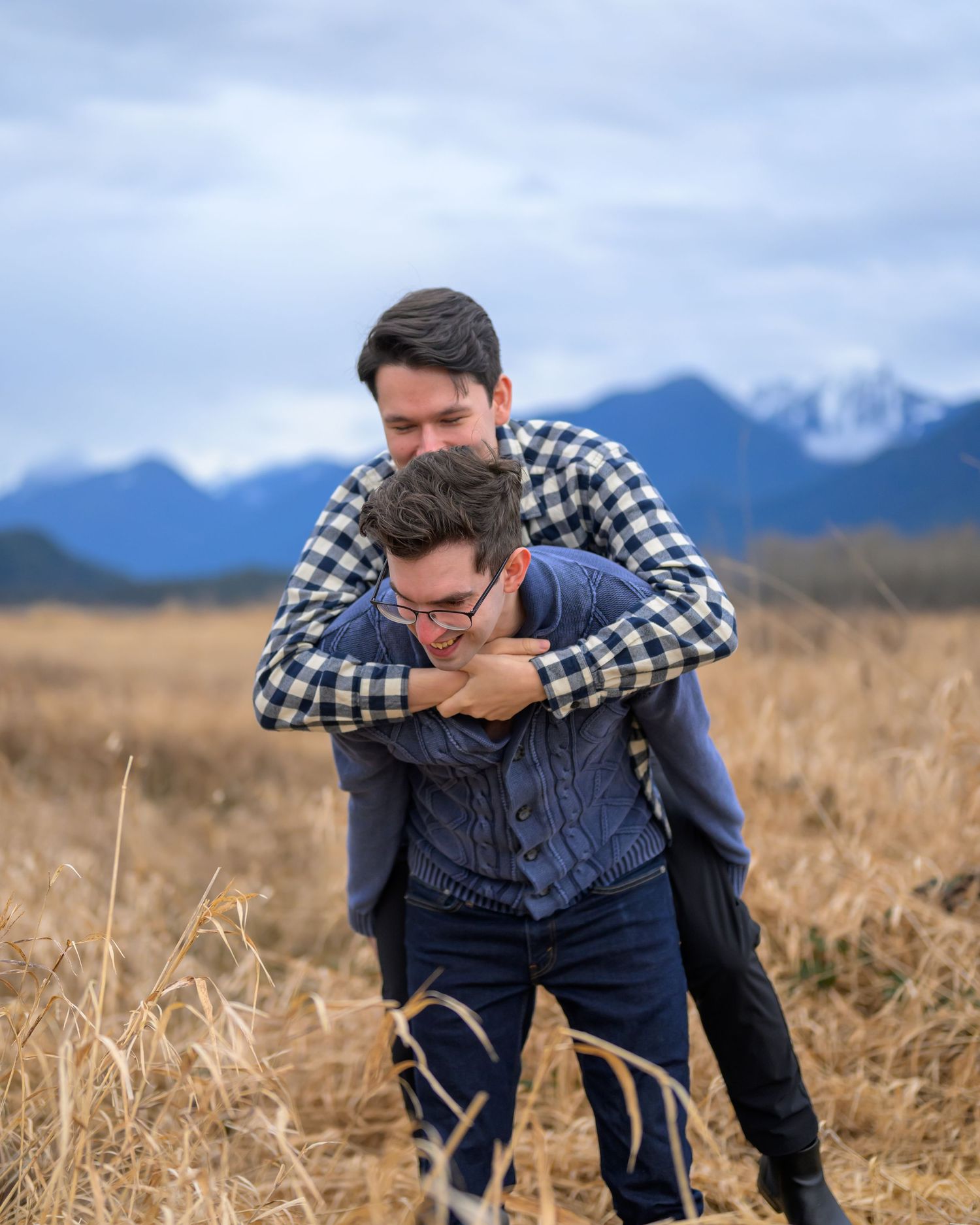 Couple in casual wear embracing in field with mountain landscape.