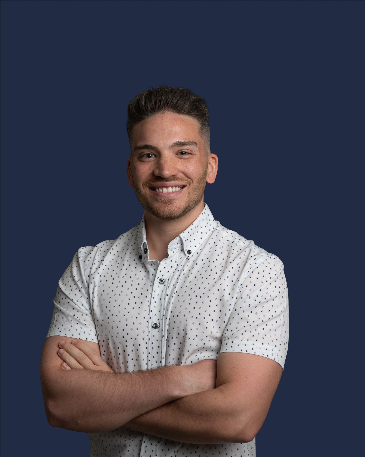Person in white polka dot shirt posing against dark blue background.