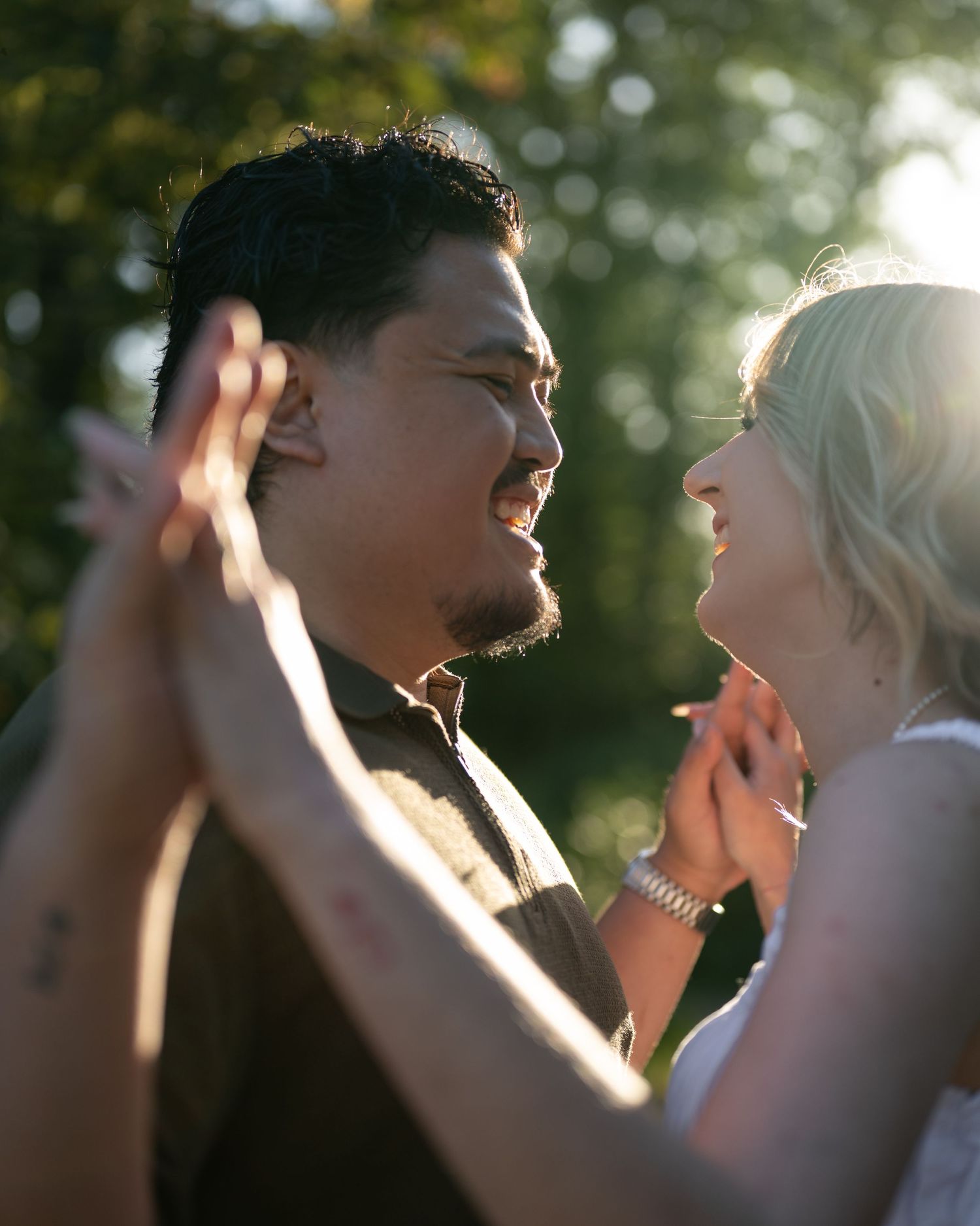 Couple sharing a romantic moment outdoors, holding hands and smiling at each other in warm golden sunlight.