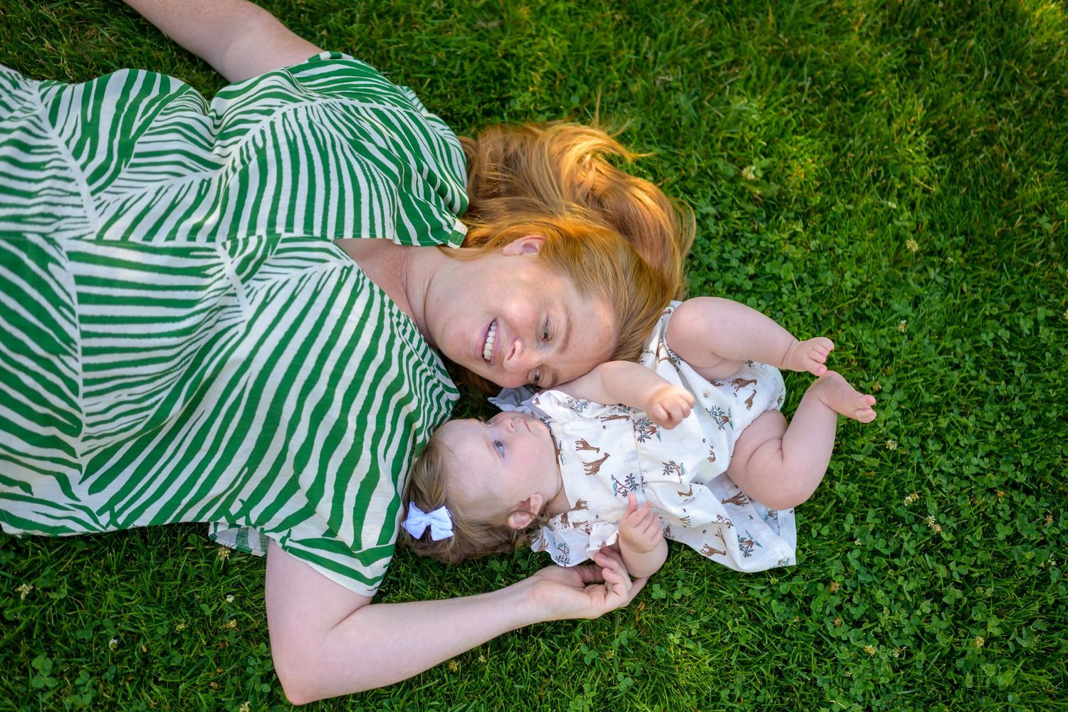 People laying on striped blanket in green grass.