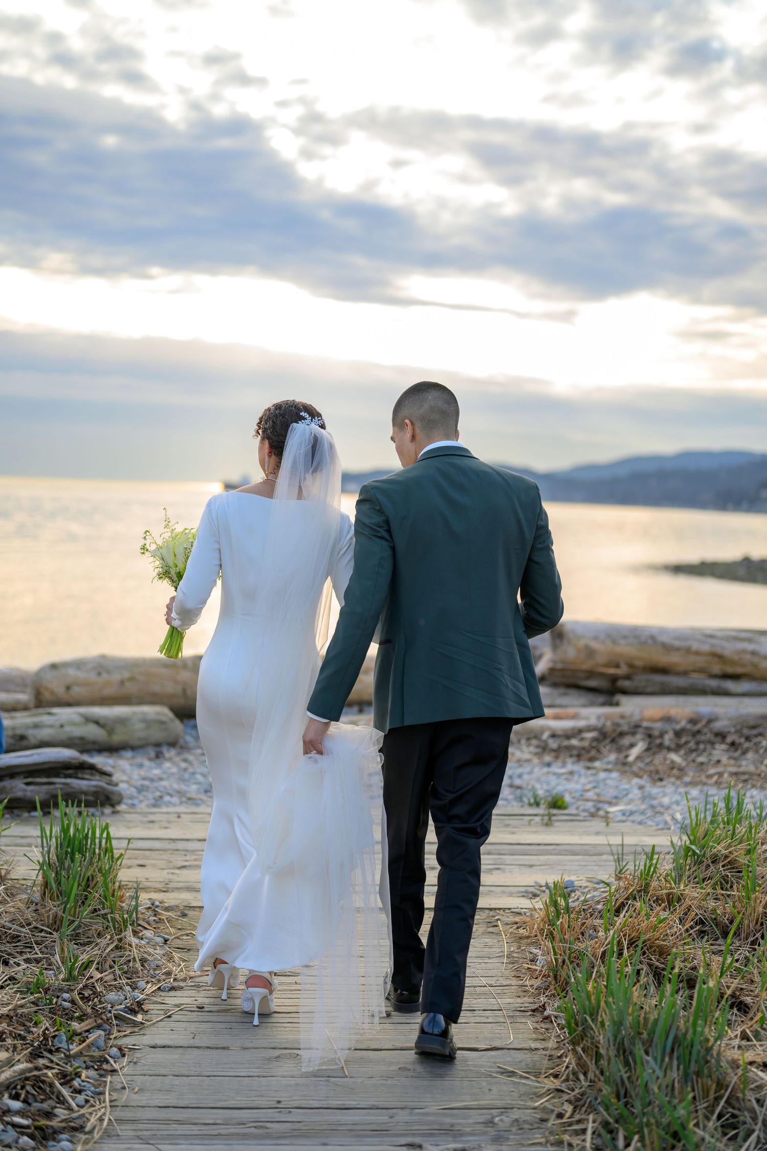 Newlyweds walking together on a coastal path during sunset with water views.