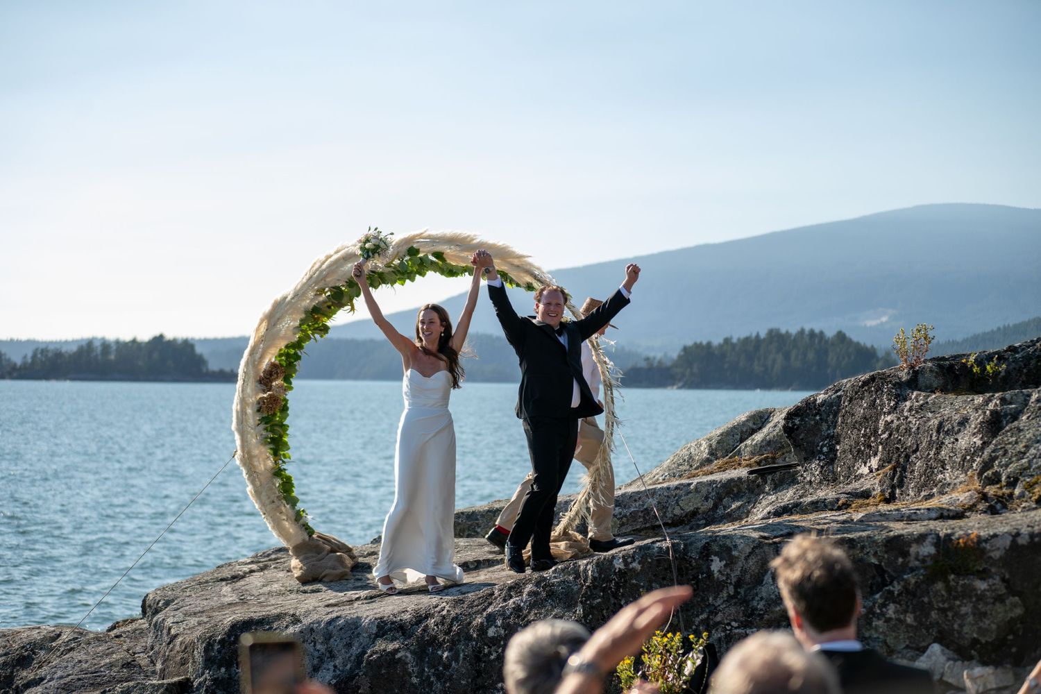 Celebratory group poses and jumps on scenic coastal rocks during wedding festivities.