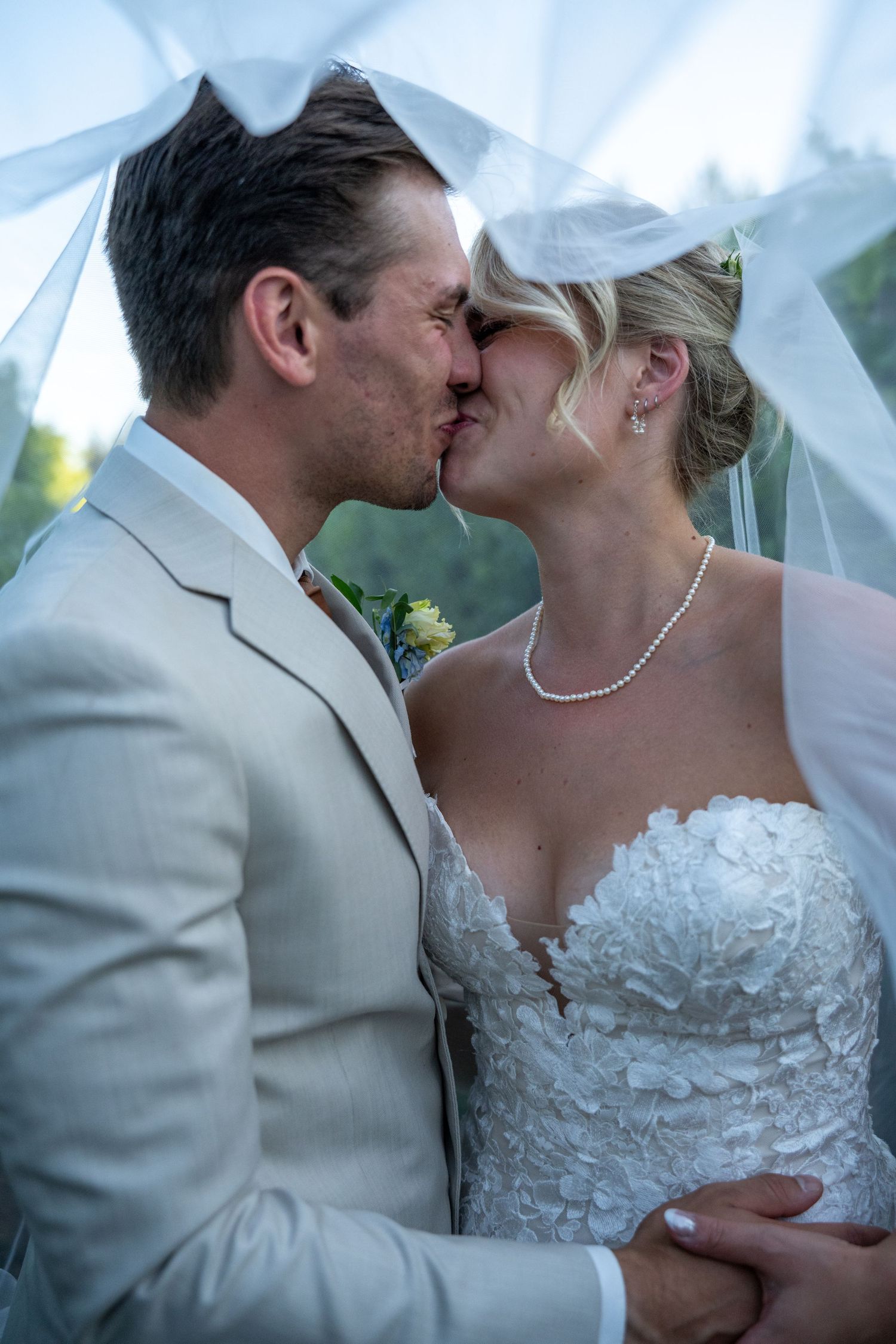 Bride and groom sharing a romantic kiss under a flowing white veil on their wedding day.