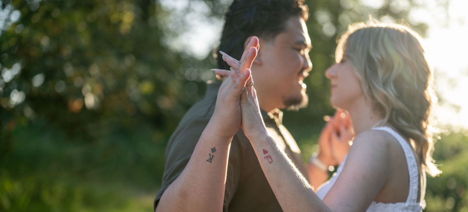 Romantic couple sharing a tender moment outdoors, with golden sunlight filtering through green trees.