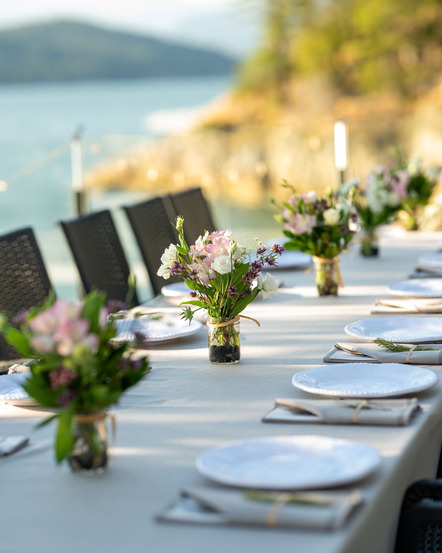 Elegant outdoor wedding reception table settings with white plates and floral centerpieces overlooking the ocean.