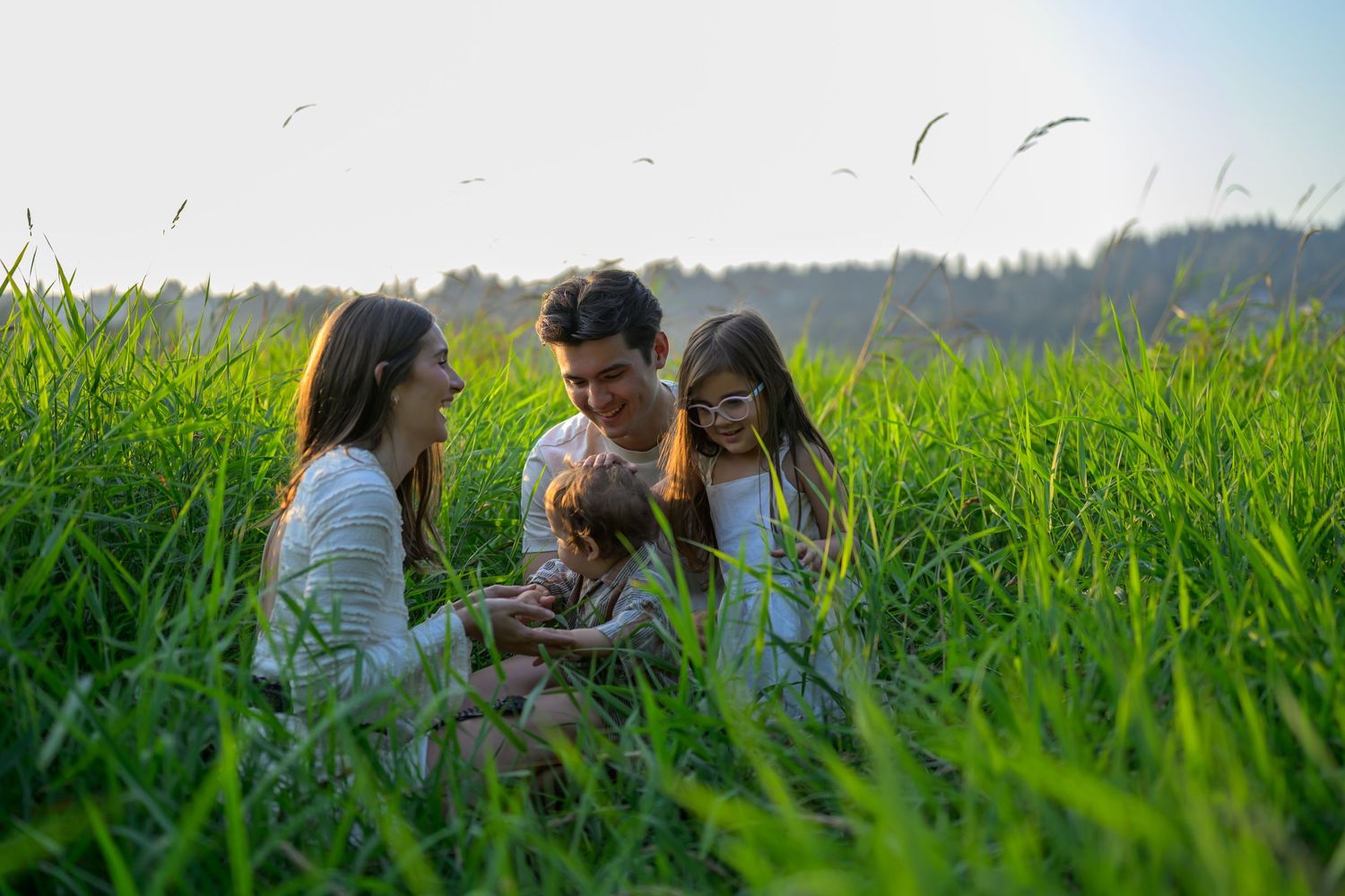 Couple lying in tall green grass field during golden hour sunset.