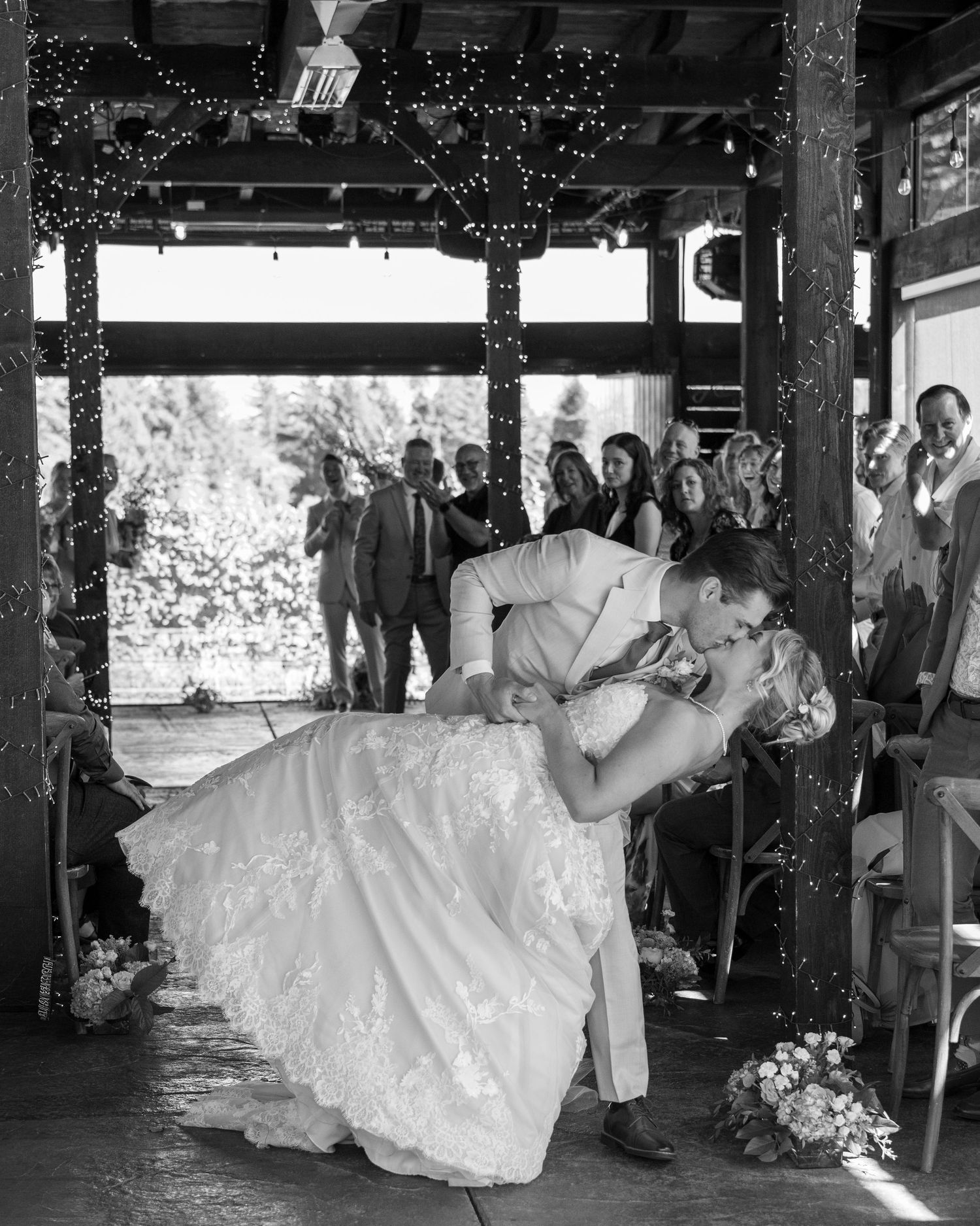Black and white photo of a groom dipping his bride for a kiss at their wedding ceremony.