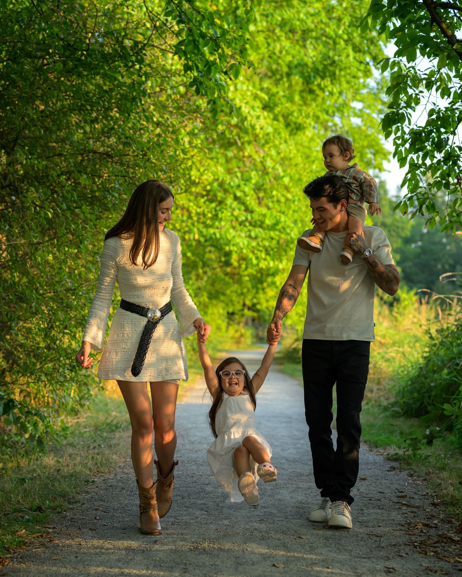 Family walking together on tree-lined path during golden hour photoshoot.