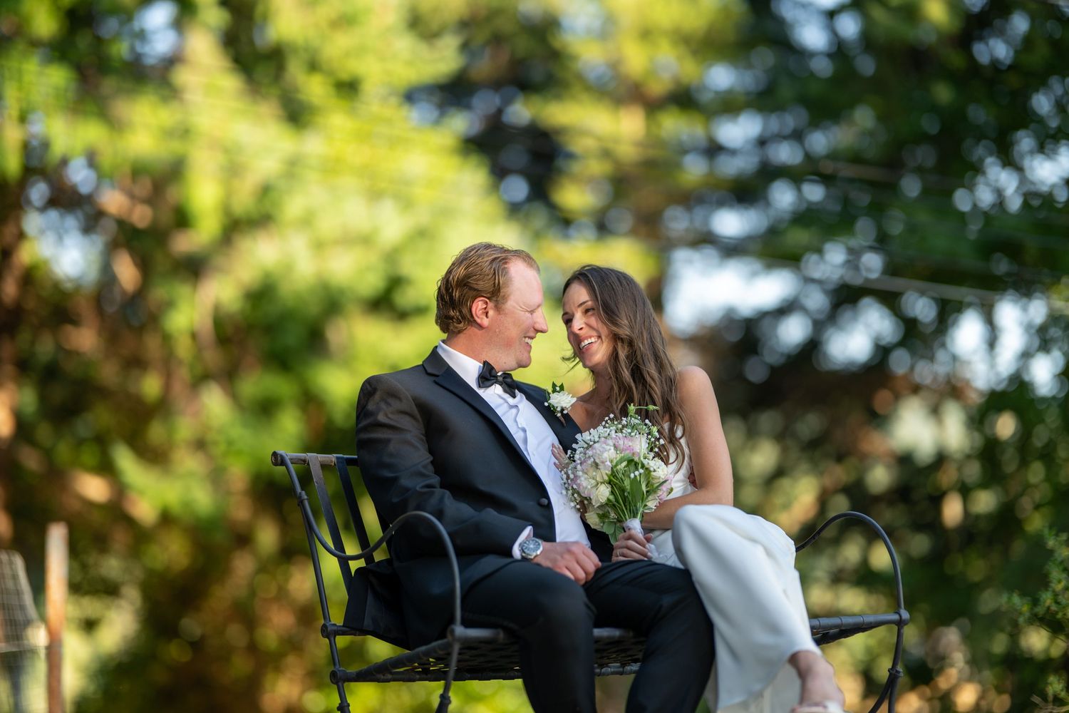 Couple in wedding attire sharing intimate moments in a sunlit garden setting with lush greenery in the background.